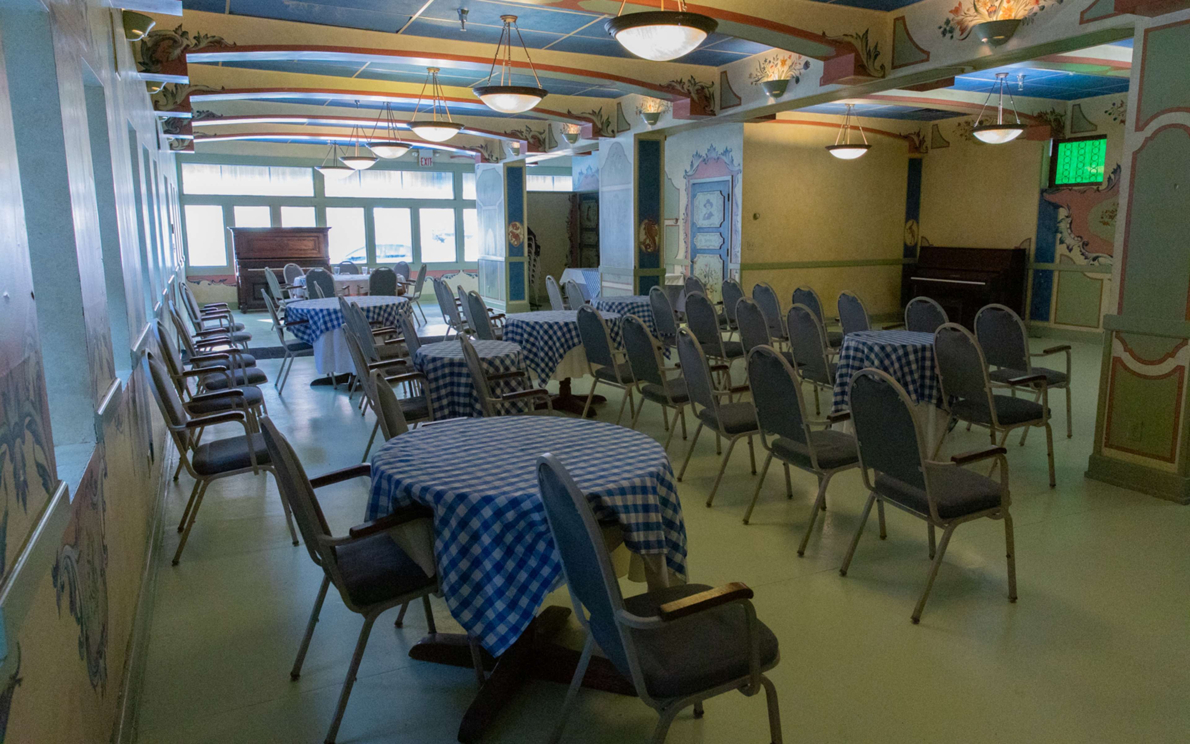An empty dining room arranged with checkered tables and chairs, featuring decorative murals on the walls.