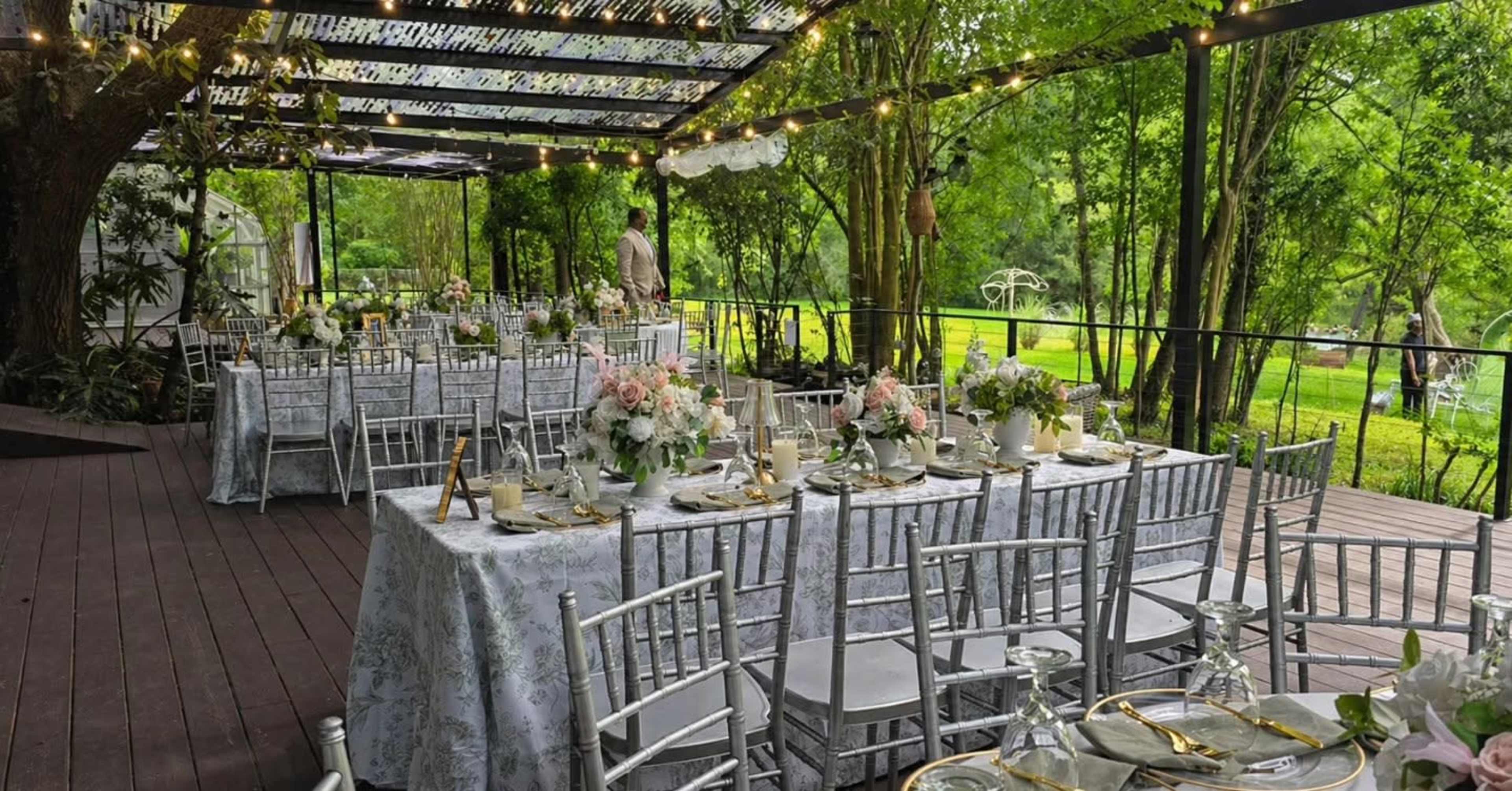The image shows a decorated outdoor wedding reception with long tables covered in floral arrangements and elegant table settings under a canopy of greenery.