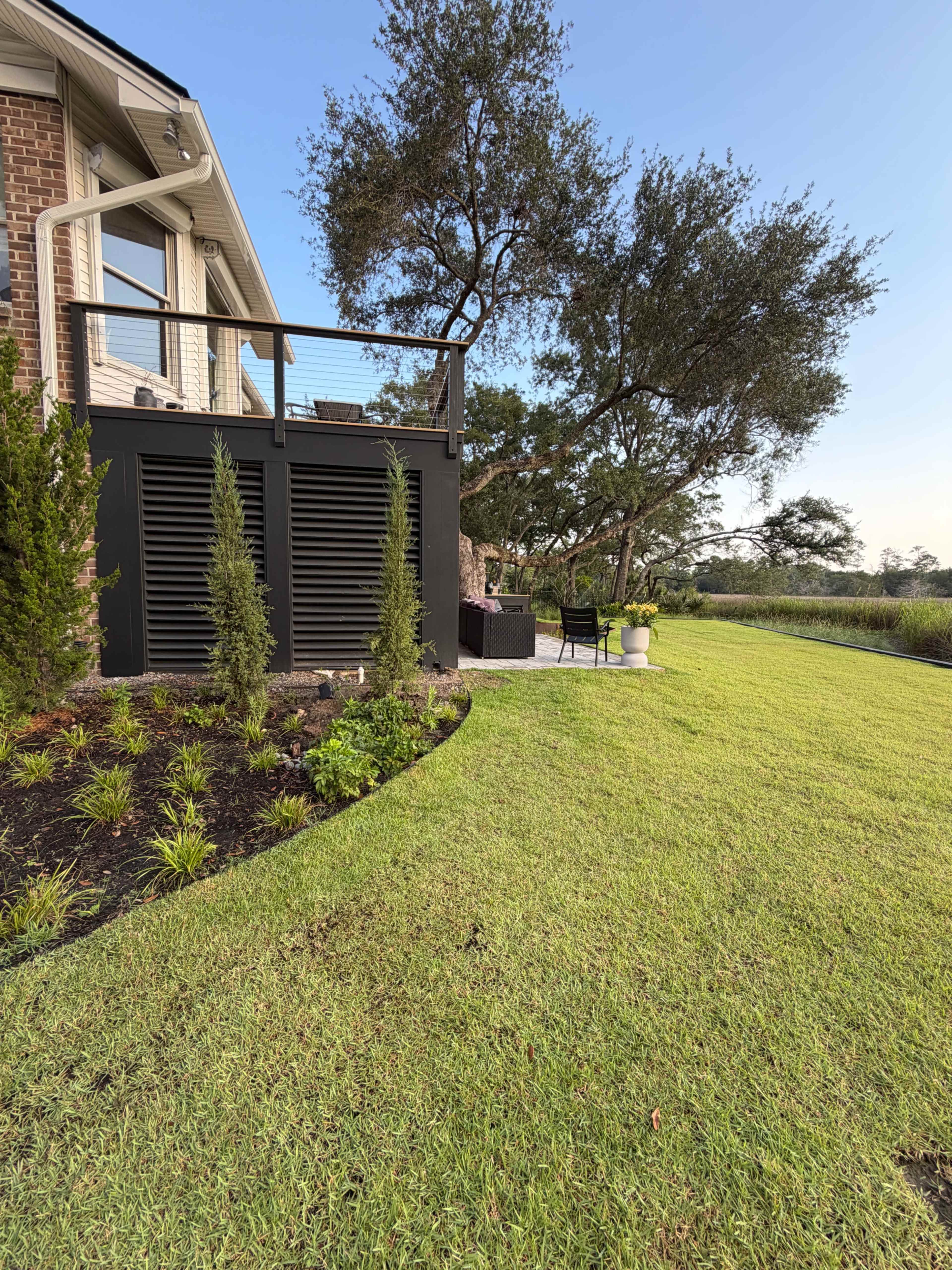 The image shows a well-maintained lawn adjacent to a house with a deck, featuring potted plants and seating areas.