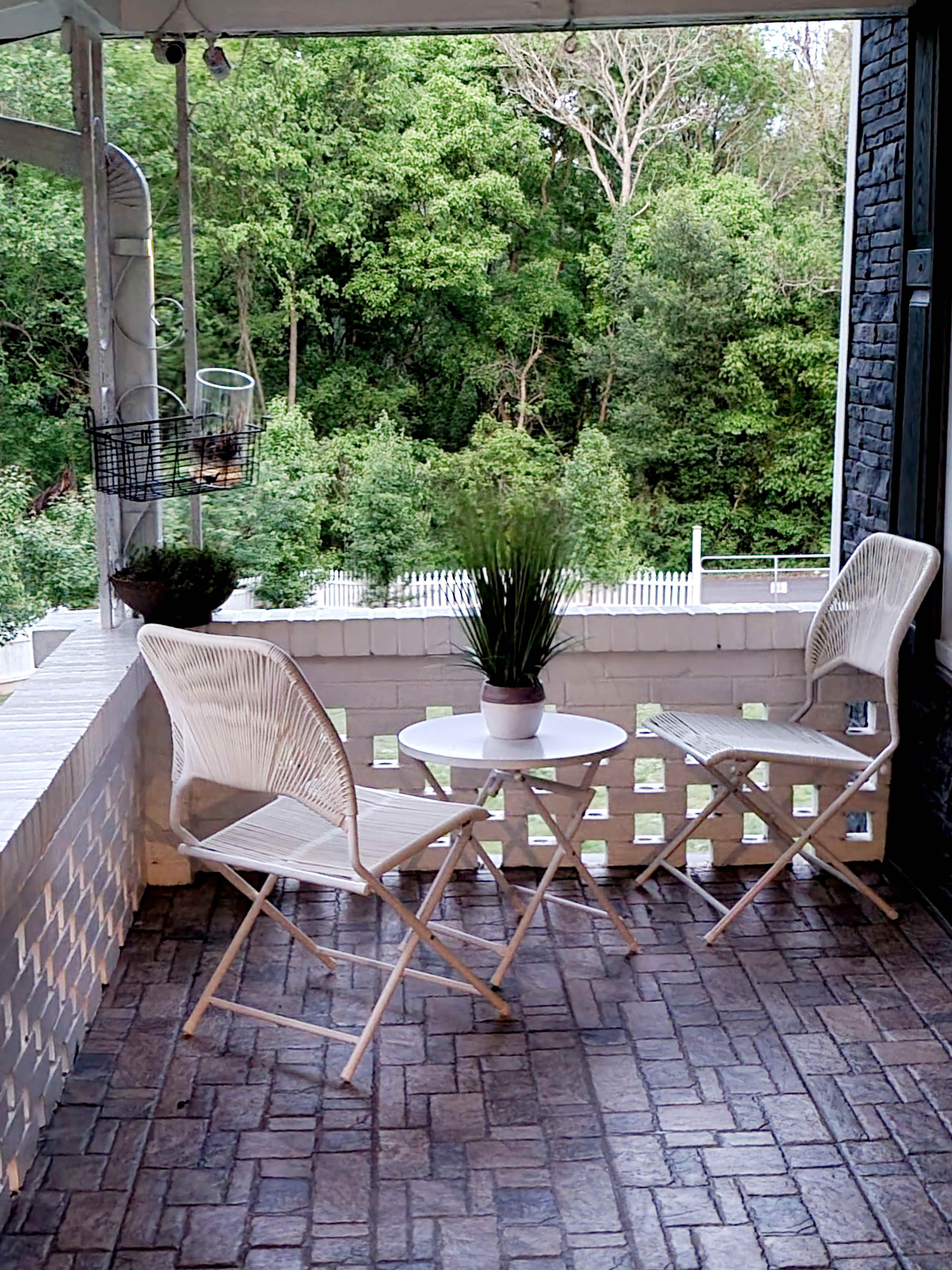 A small balcony features two folding chairs and a round table, overlooking a lush green landscape.