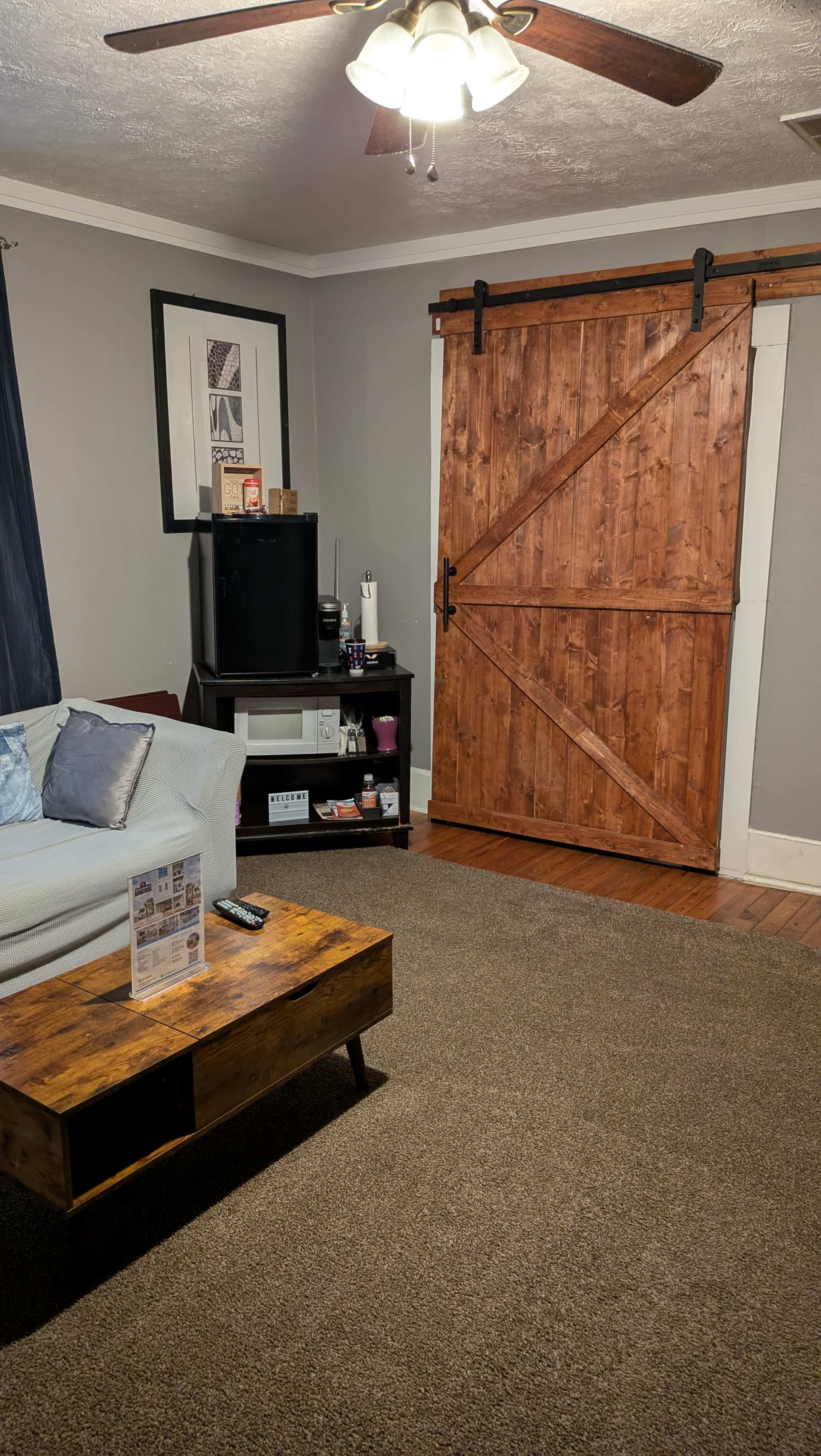 The living room features a light-colored sofa, a wooden coffee table, and a large sliding barn door made of wood.