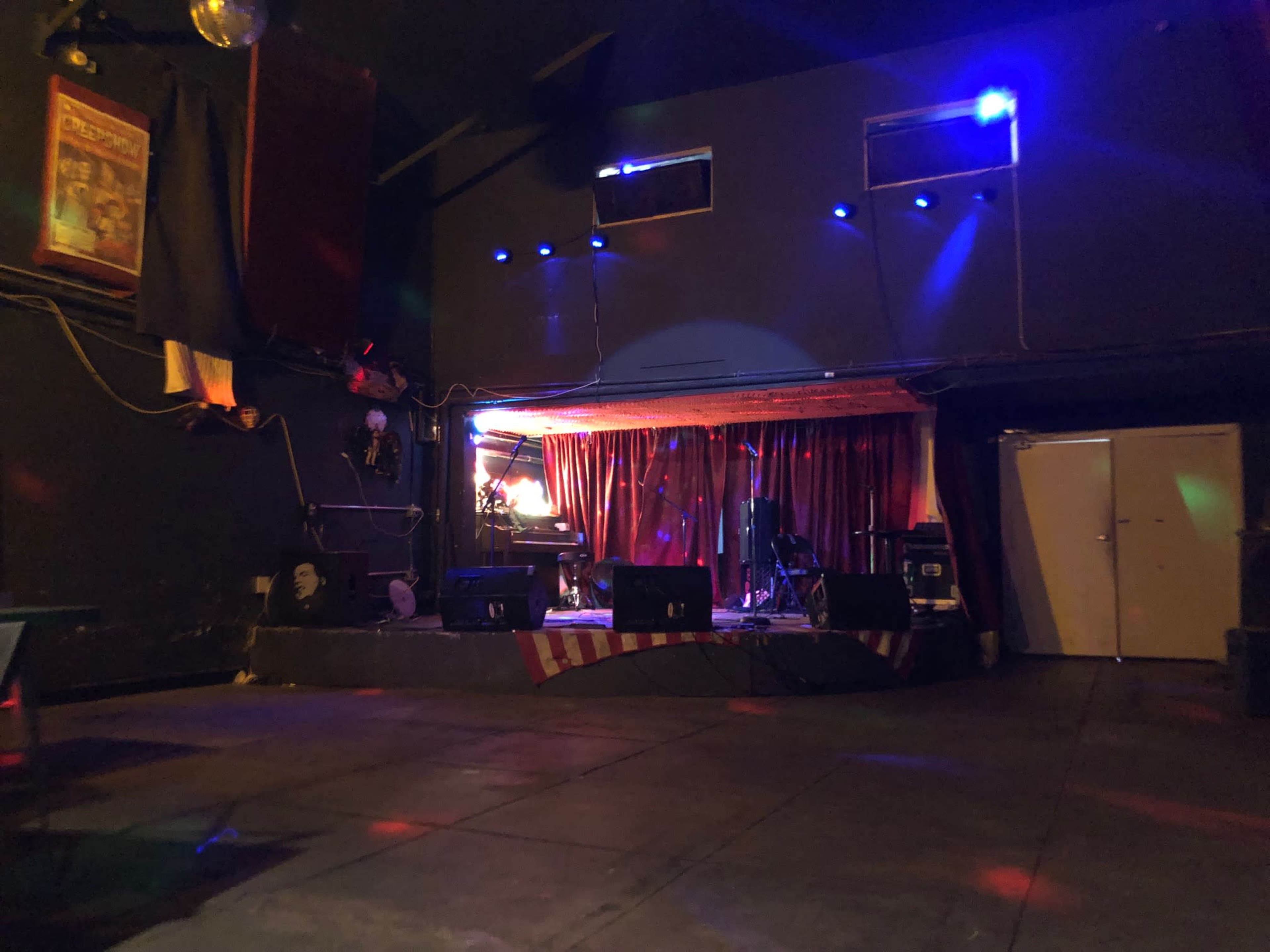 A dimly lit stage area in a music venue, featuring a performance space with curtains and musical equipment set up.