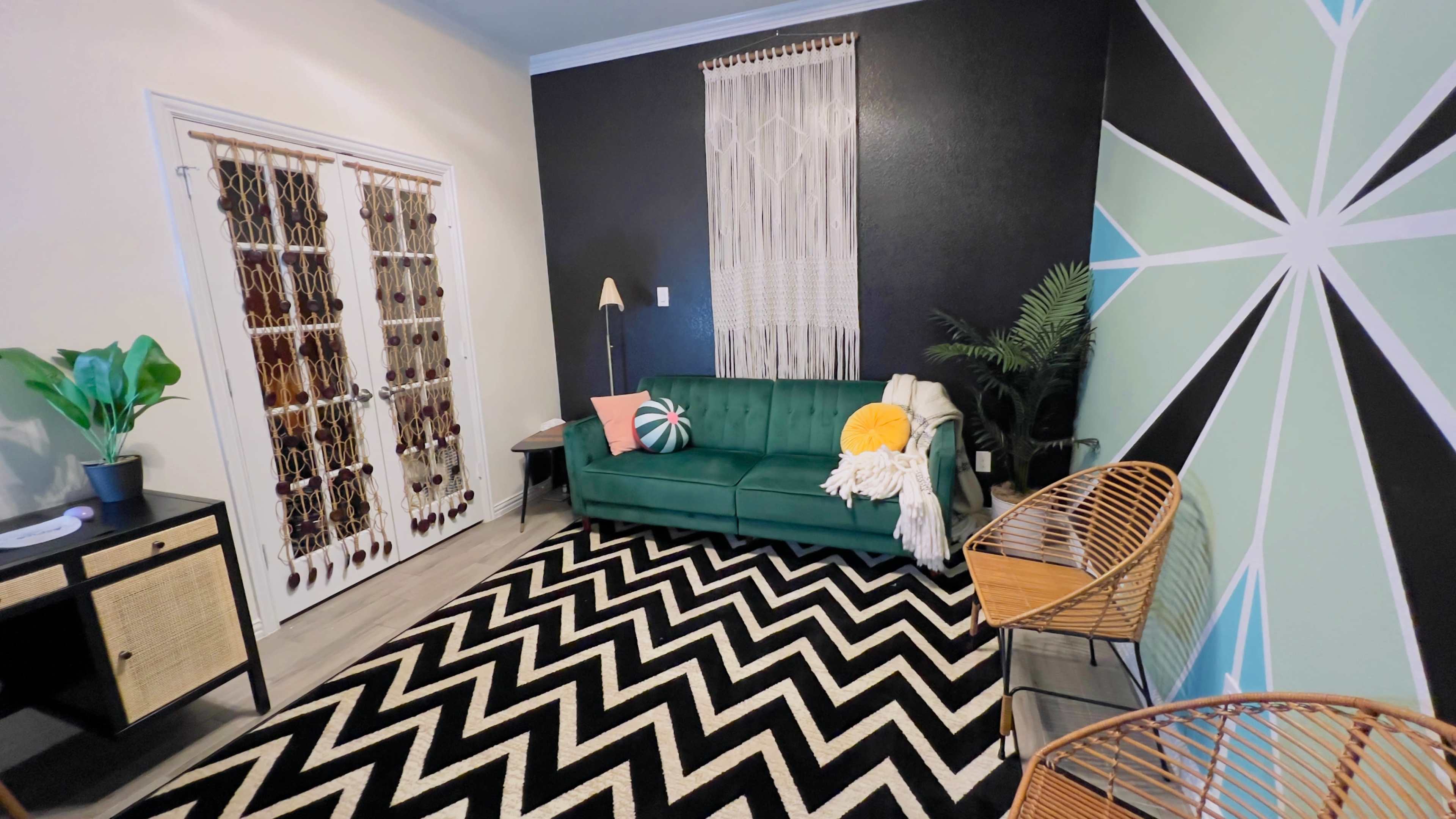 A modern living room with a green sofa, a chevron-patterned black and white rug, and a colorful geometric wall mural.