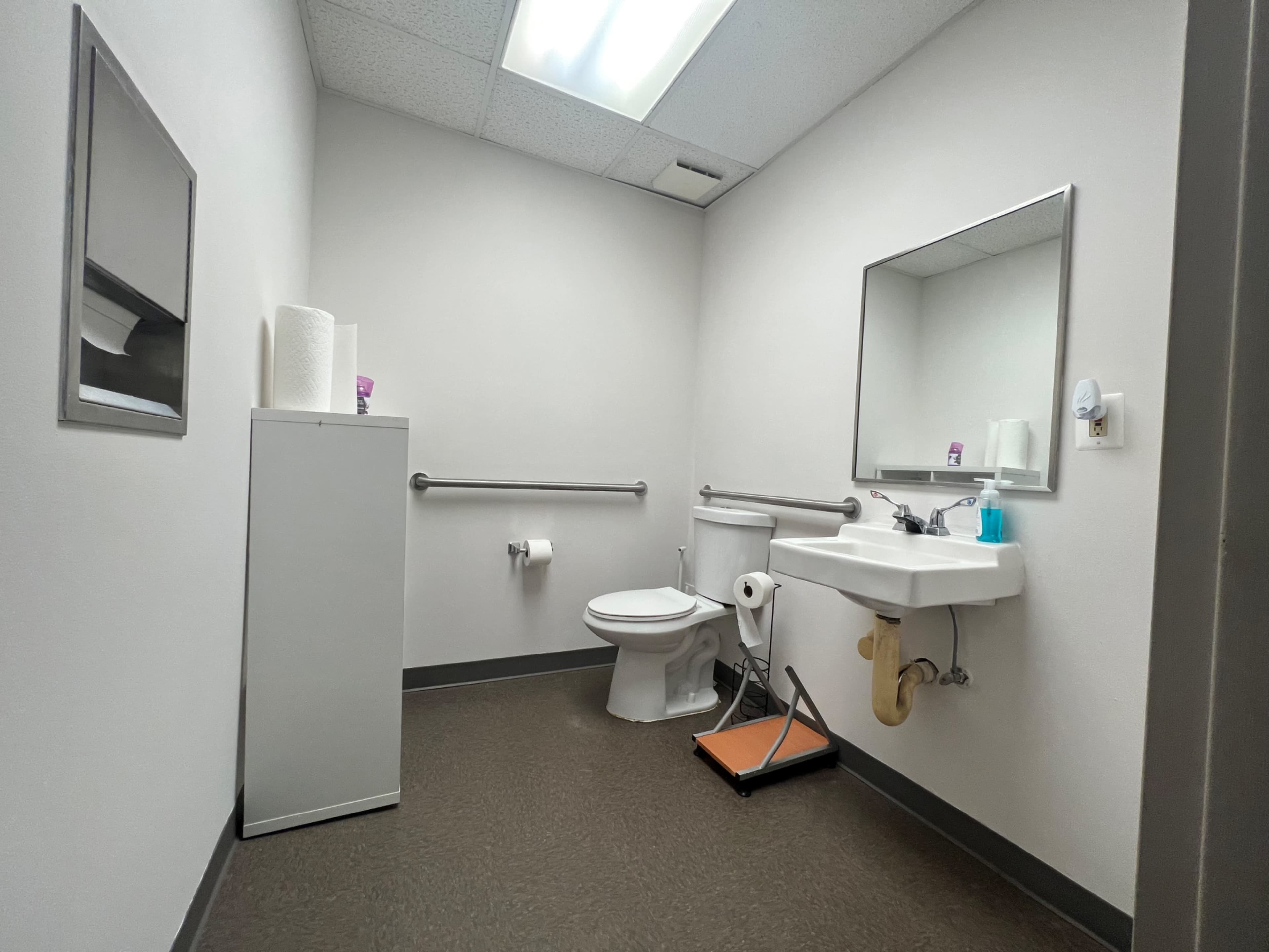 A clean restroom with a toilet, sink, a roll of paper towels, and a wall-mounted mirror.
