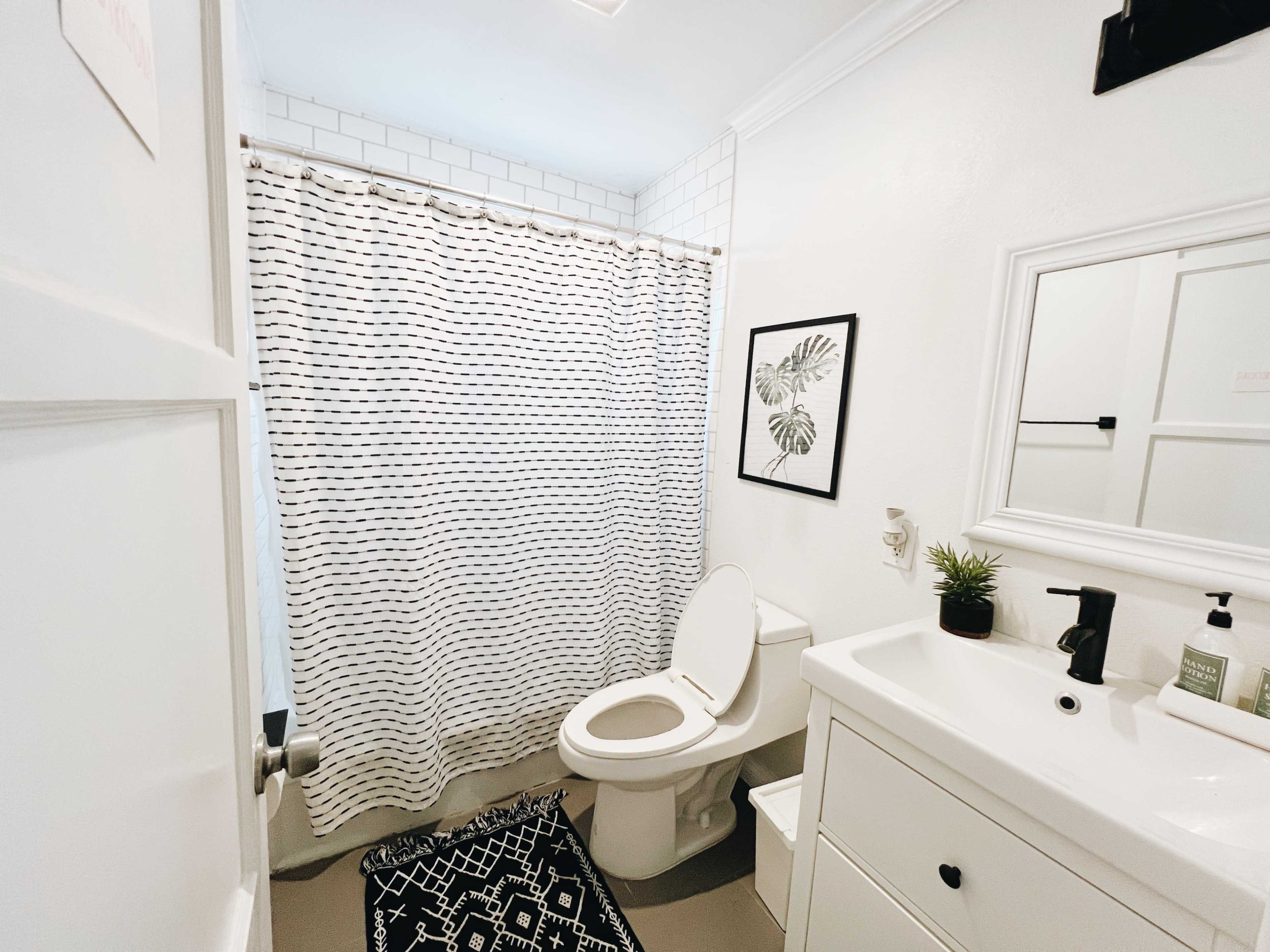 A bathroom with a shower curtain, toilet, sink with a mirror, and a decorative rug.