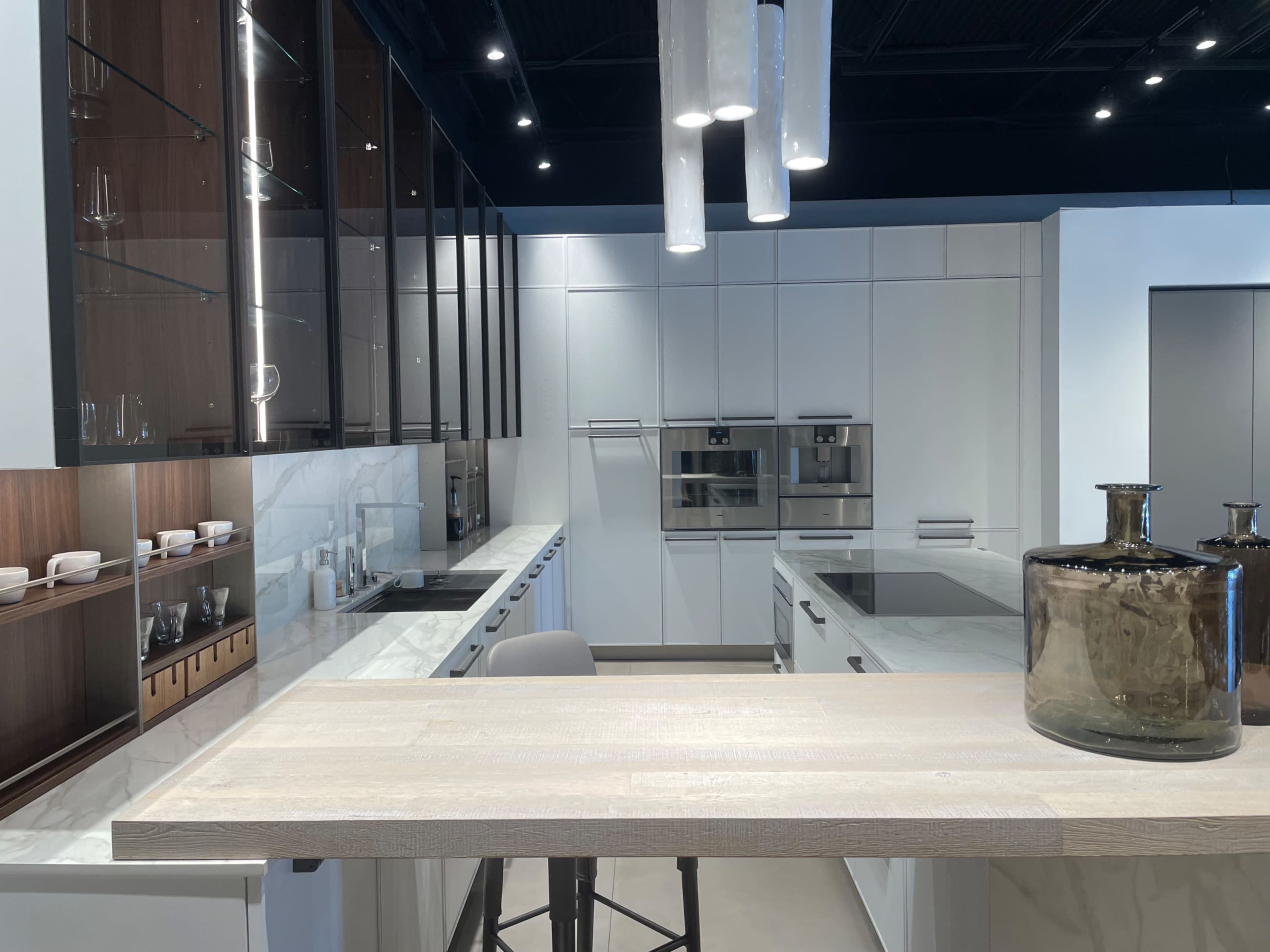 A modern kitchen with white cabinetry, a central island, and glass display shelves.