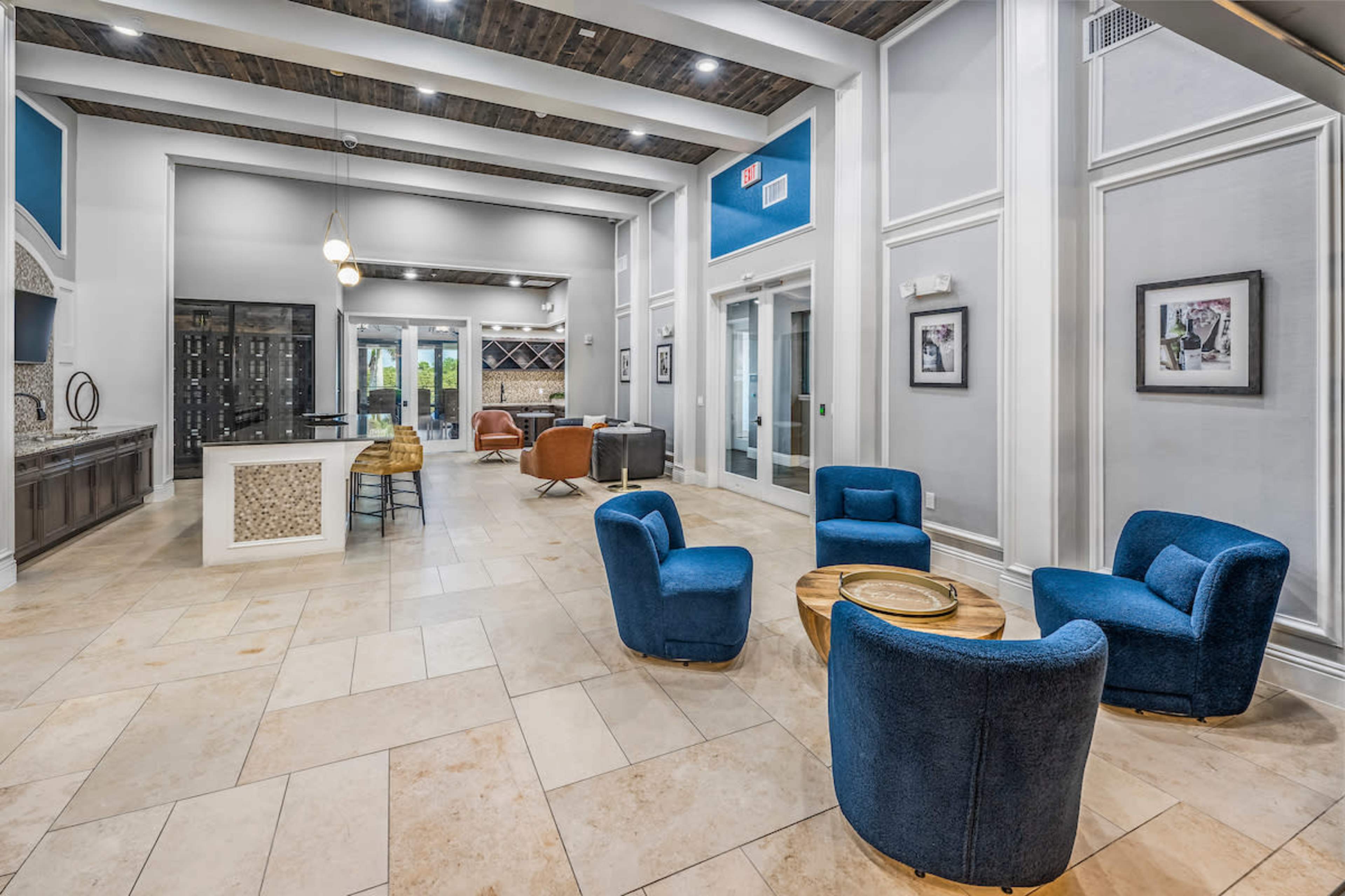 The image shows a modern lobby with four blue armchairs arranged around a wooden table, a reception area in the background, and decorative wall features.