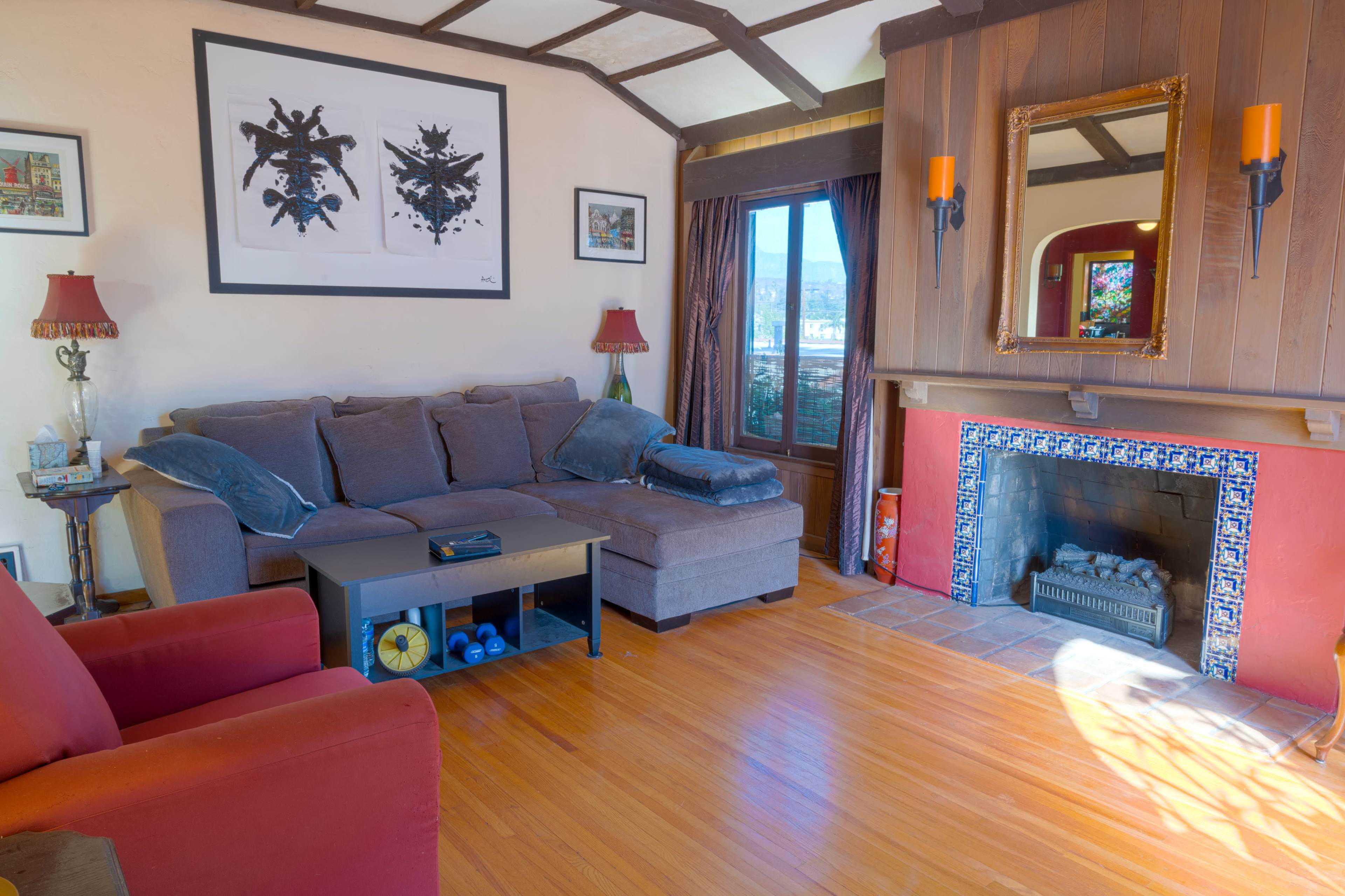 The living room features a brown couch, a red armchair, a coffee table, and a fireplace with artwork on the walls and a window offering a view.