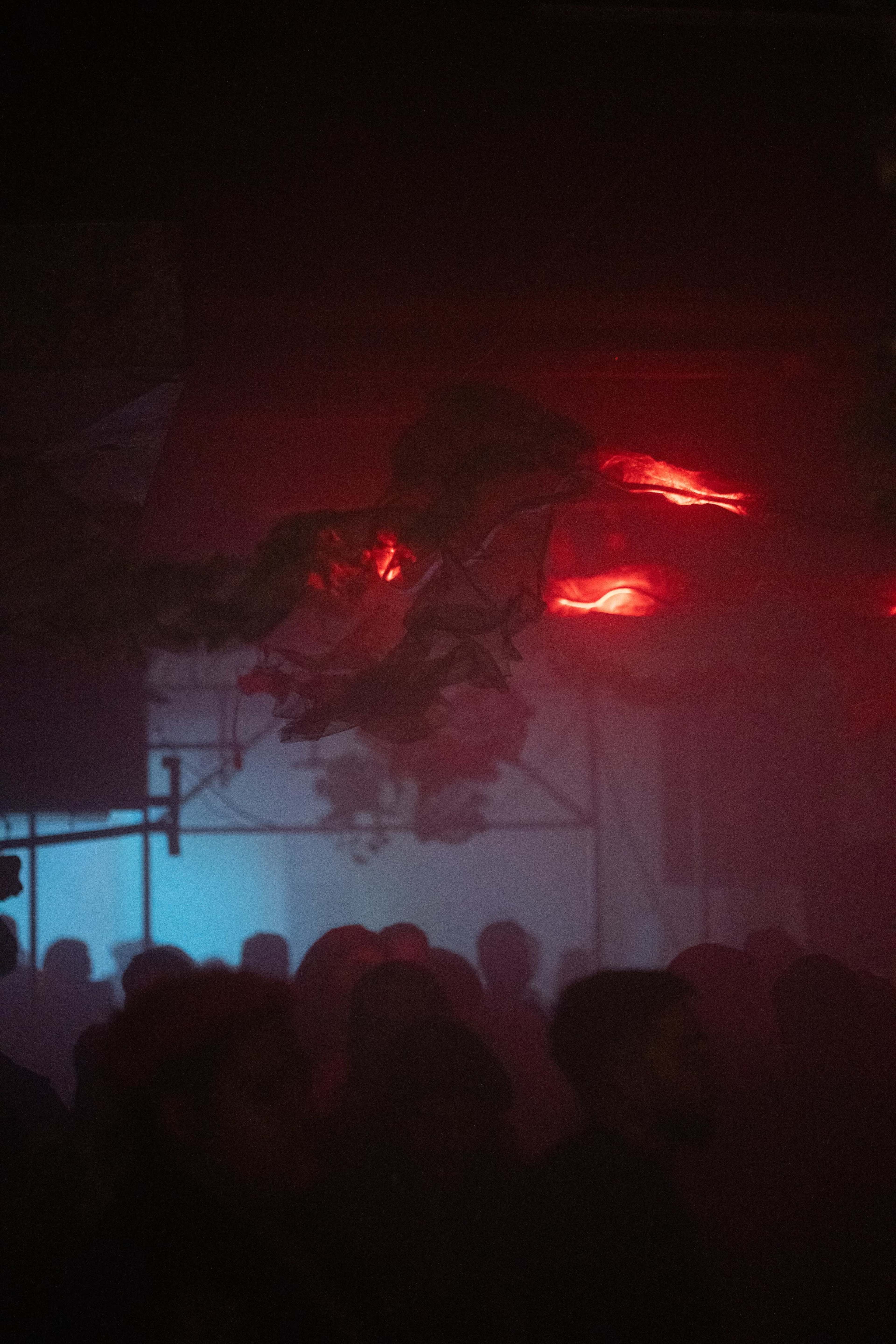 The image depicts a dimly lit scene with figures silhouetted against a backdrop of colorful lighting and fog.