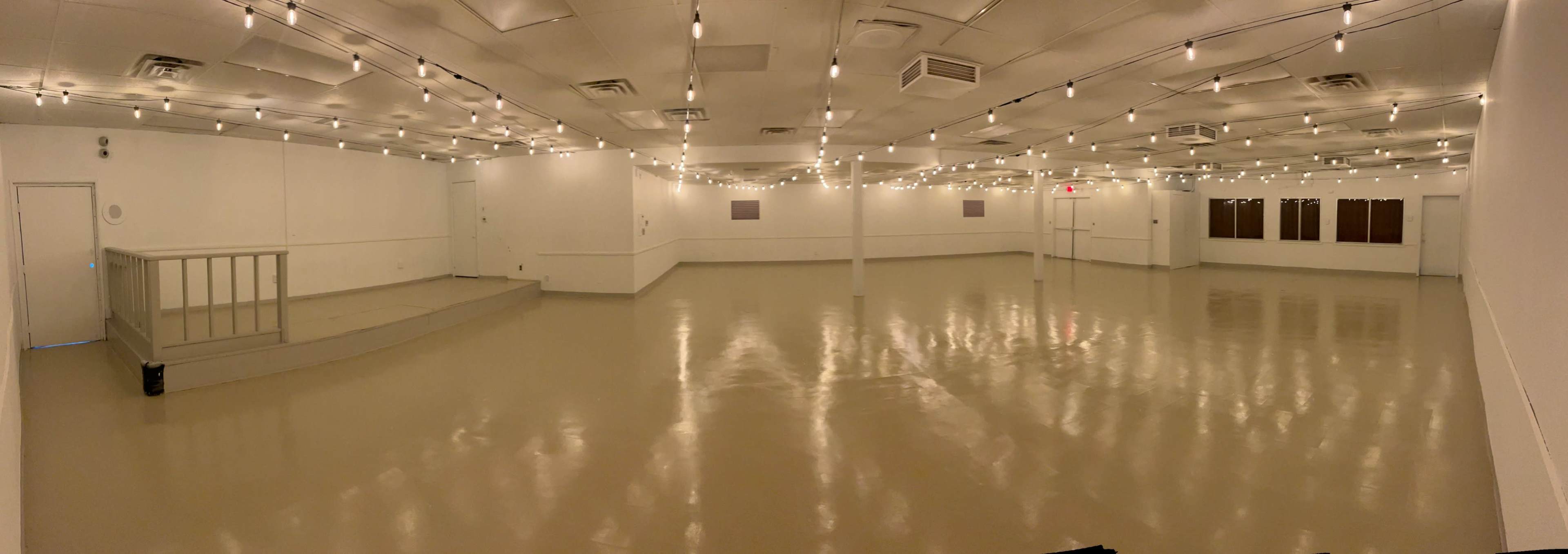 A large, empty, and brightly lit event space with string lights hanging from the ceiling and smooth, reflective flooring.
