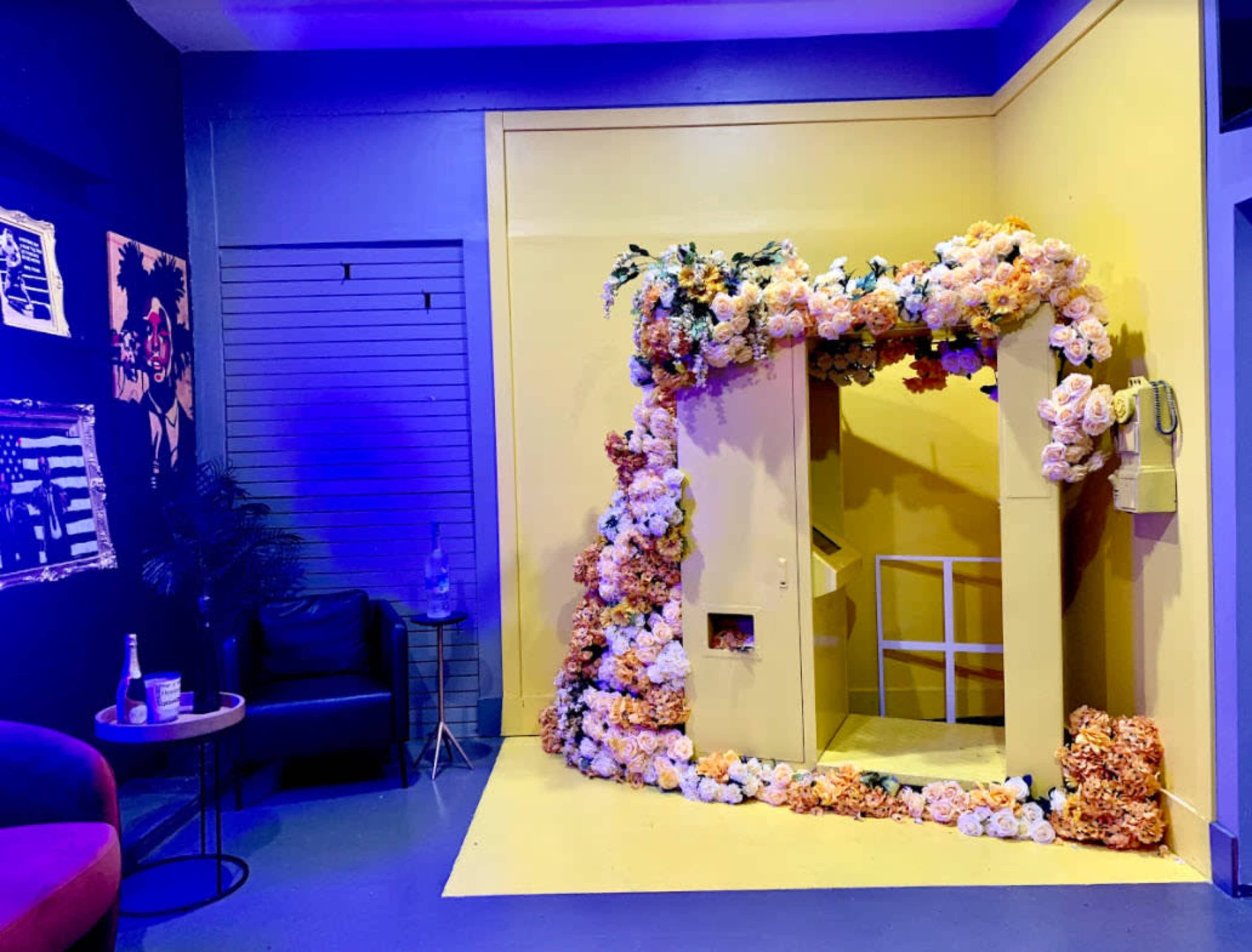 A bright yellow booth adorned with colorful flowers is situated in a room with blue walls and a small seating area.
