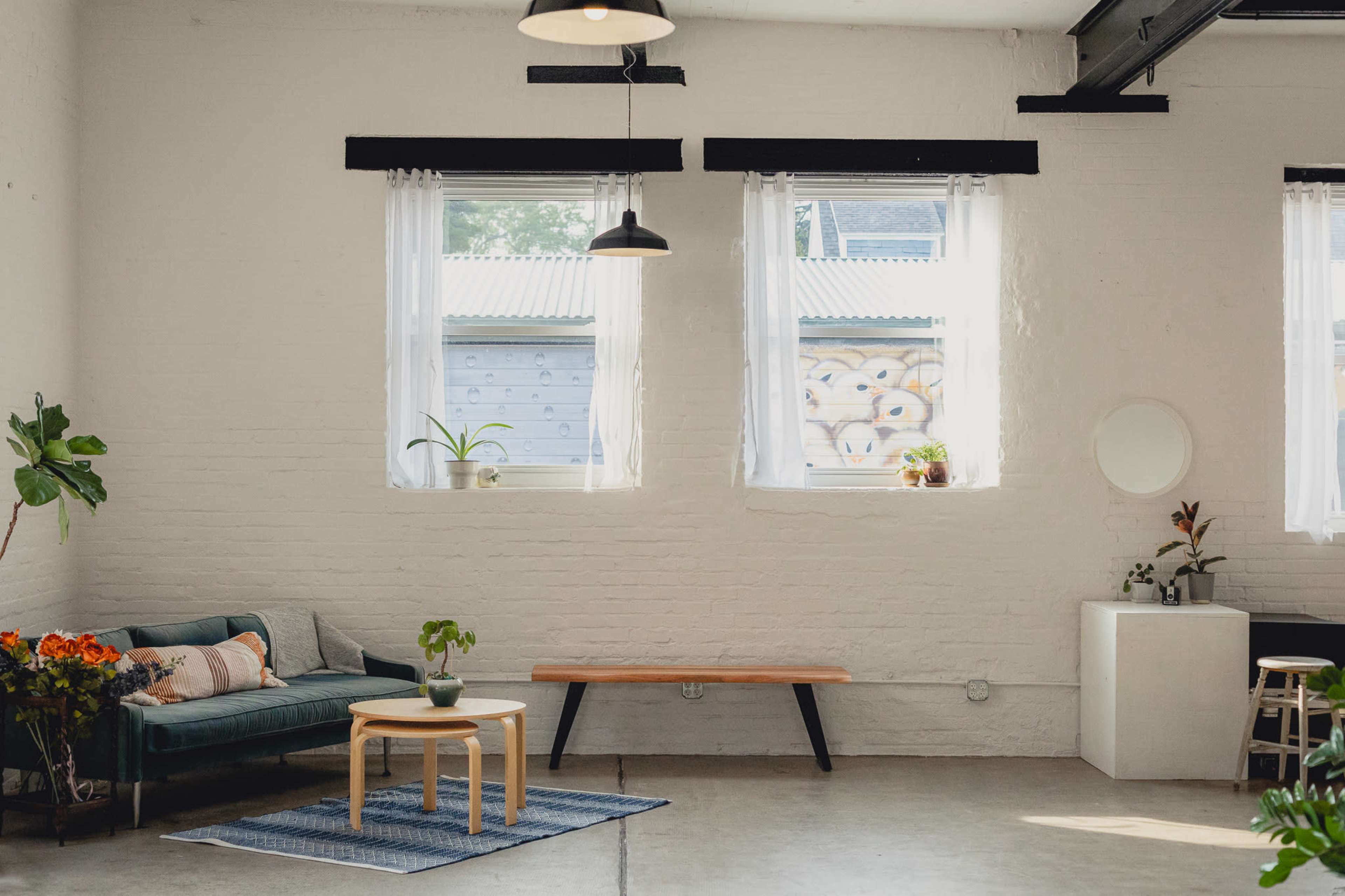 A bright and minimalistic room with large windows, a green sofa, a wooden coffee table, and a small dining area.