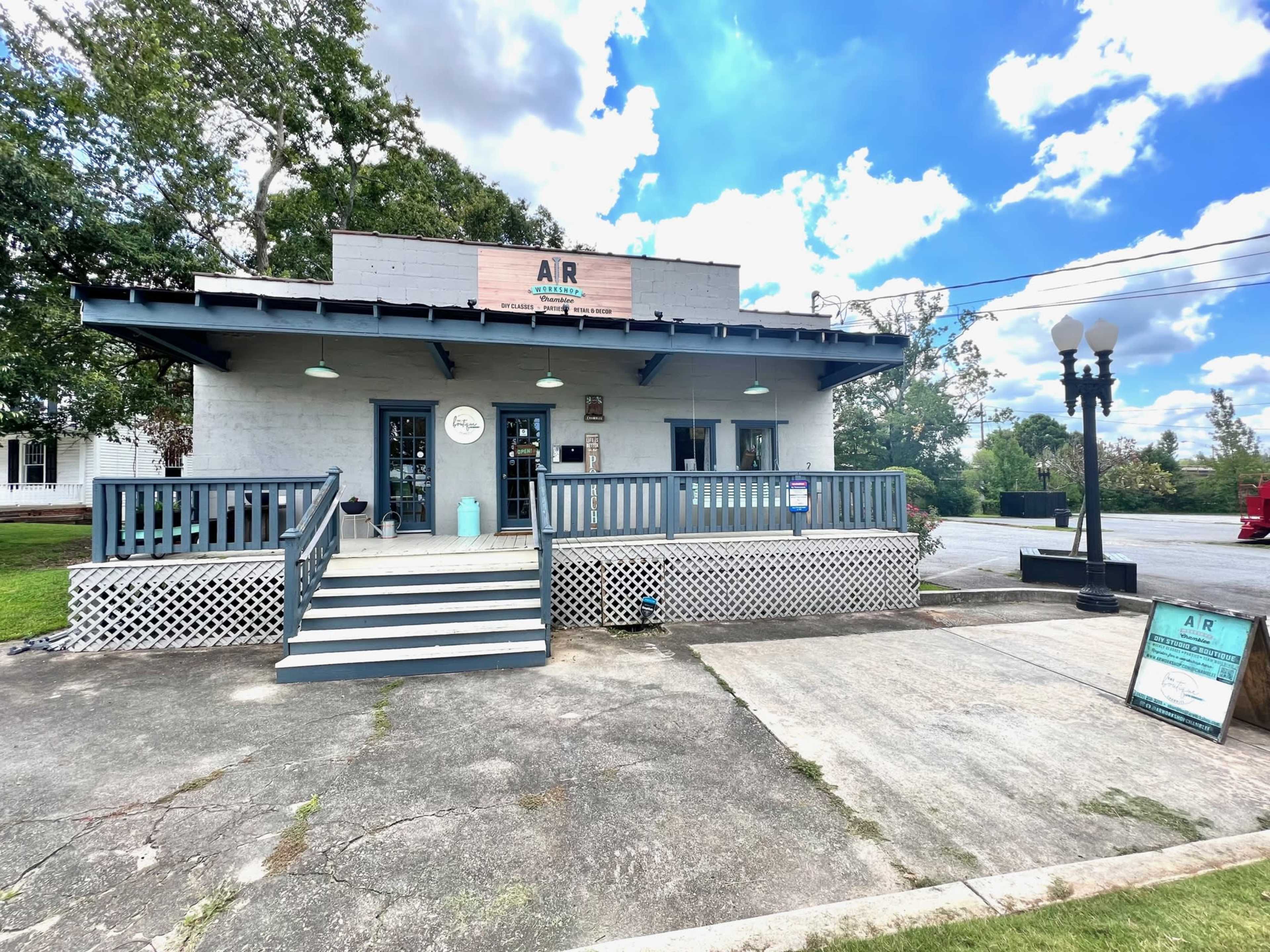 A blue-accented storefront with a porch, signage above the door, and a paved walkway leading up to the entrance, set against a partly cloudy sky.