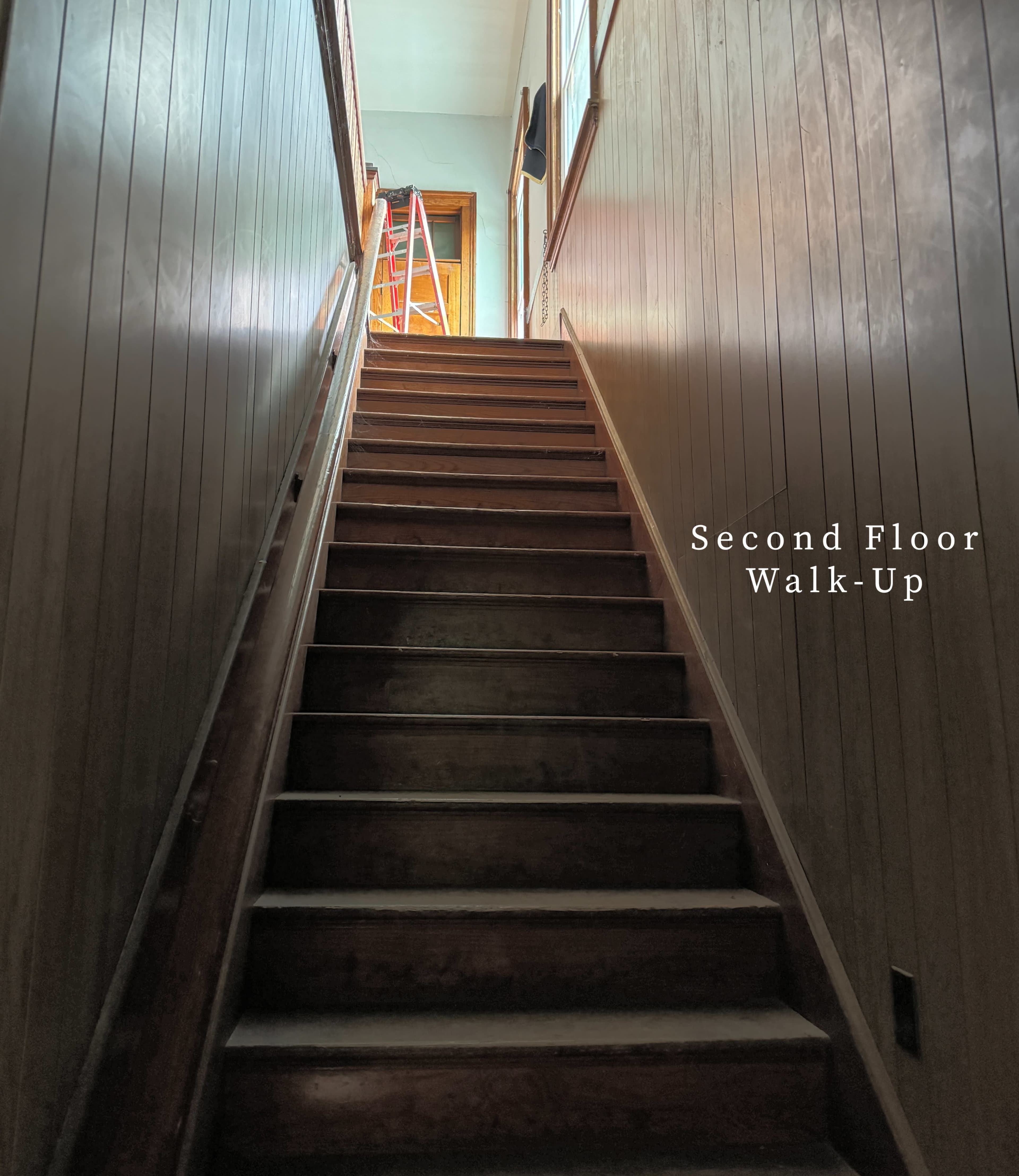 A wooden staircase leads up to a doorway illuminated by natural light, with a ladder visible near the top.