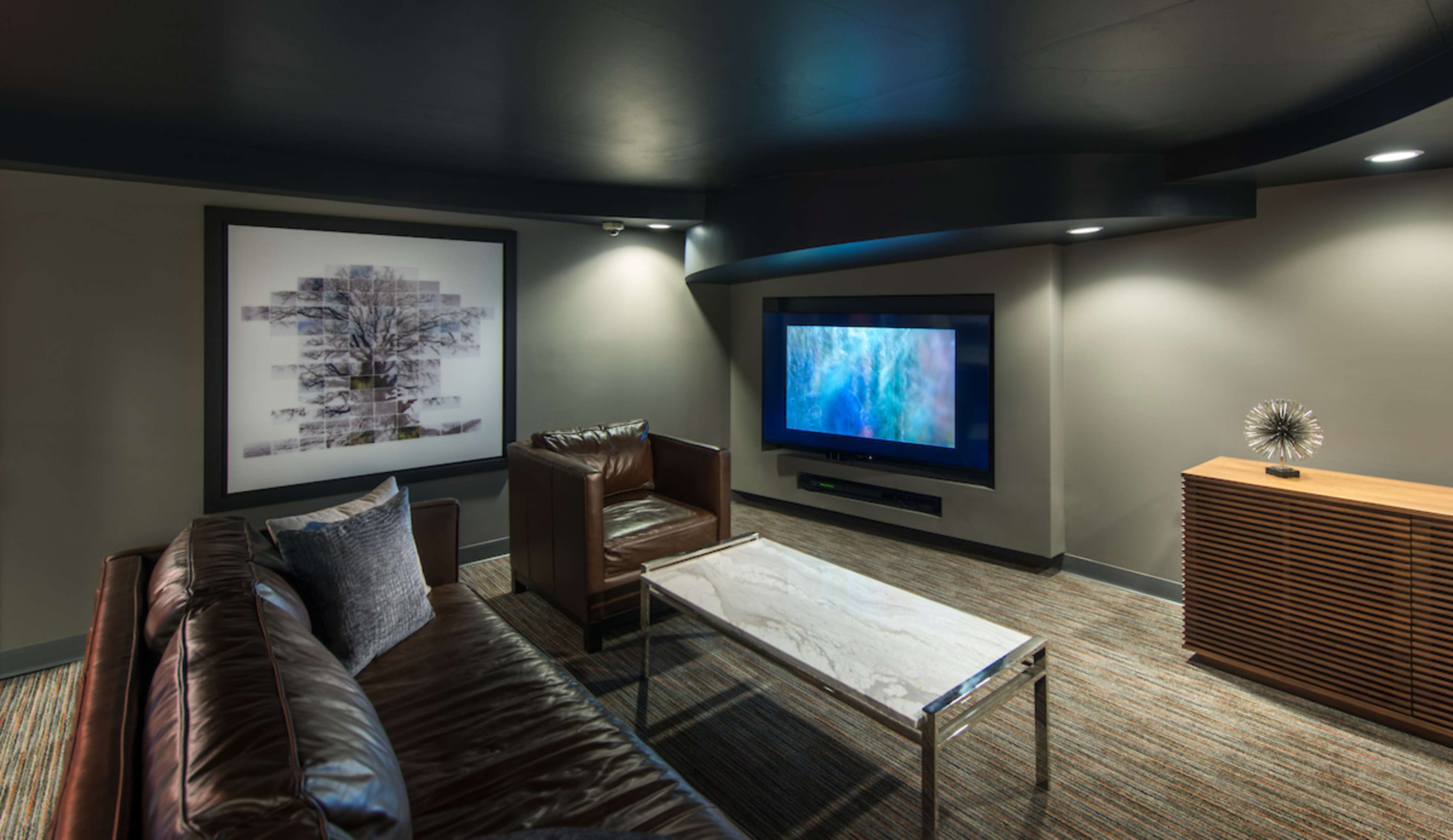 A modern living room with a leather sofa, two armchairs, a marble coffee table, a flat-screen television, and decorative artwork on the wall.