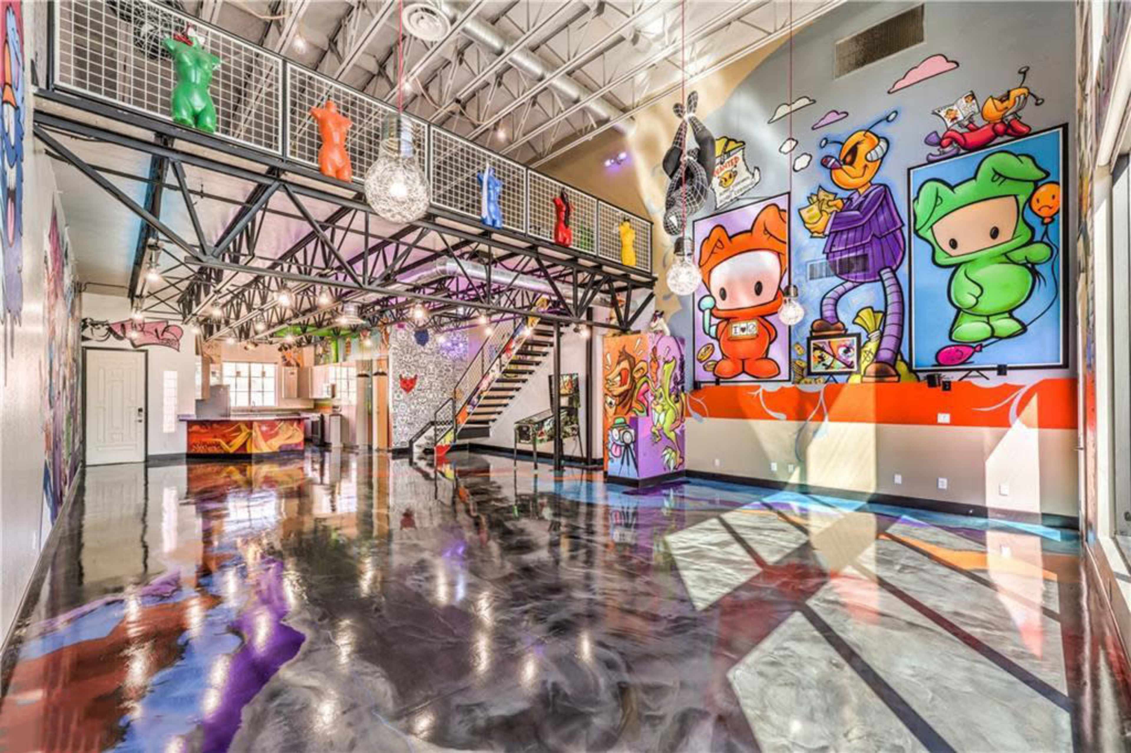 The image shows a colorful interior space featuring vibrant murals, shiny polished floors, and an open layout with a staircase and a bar area.