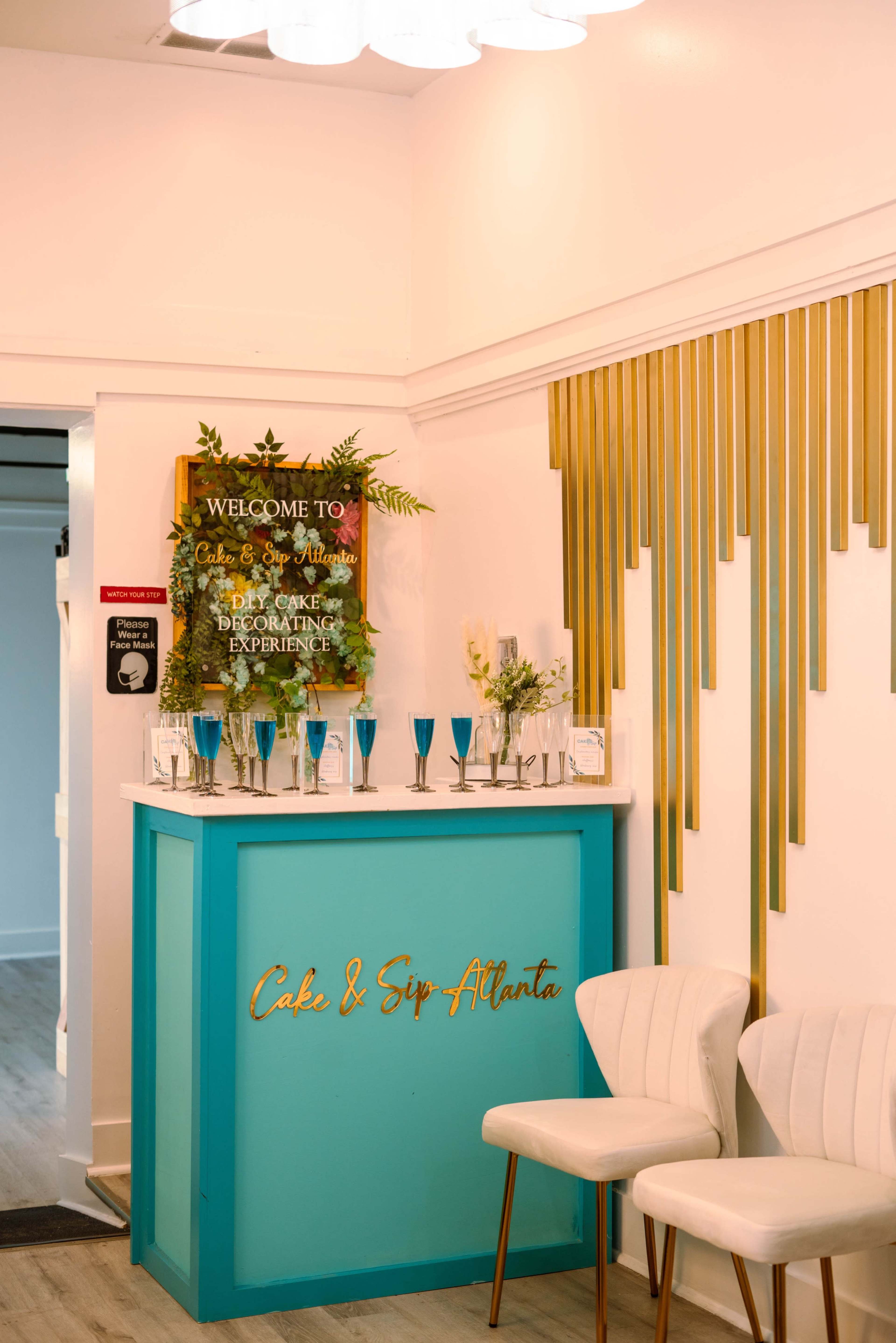 A brightly colored reception area with a turquoise counter featuring decorative glasses, a welcome sign, and gold accents on the wall.