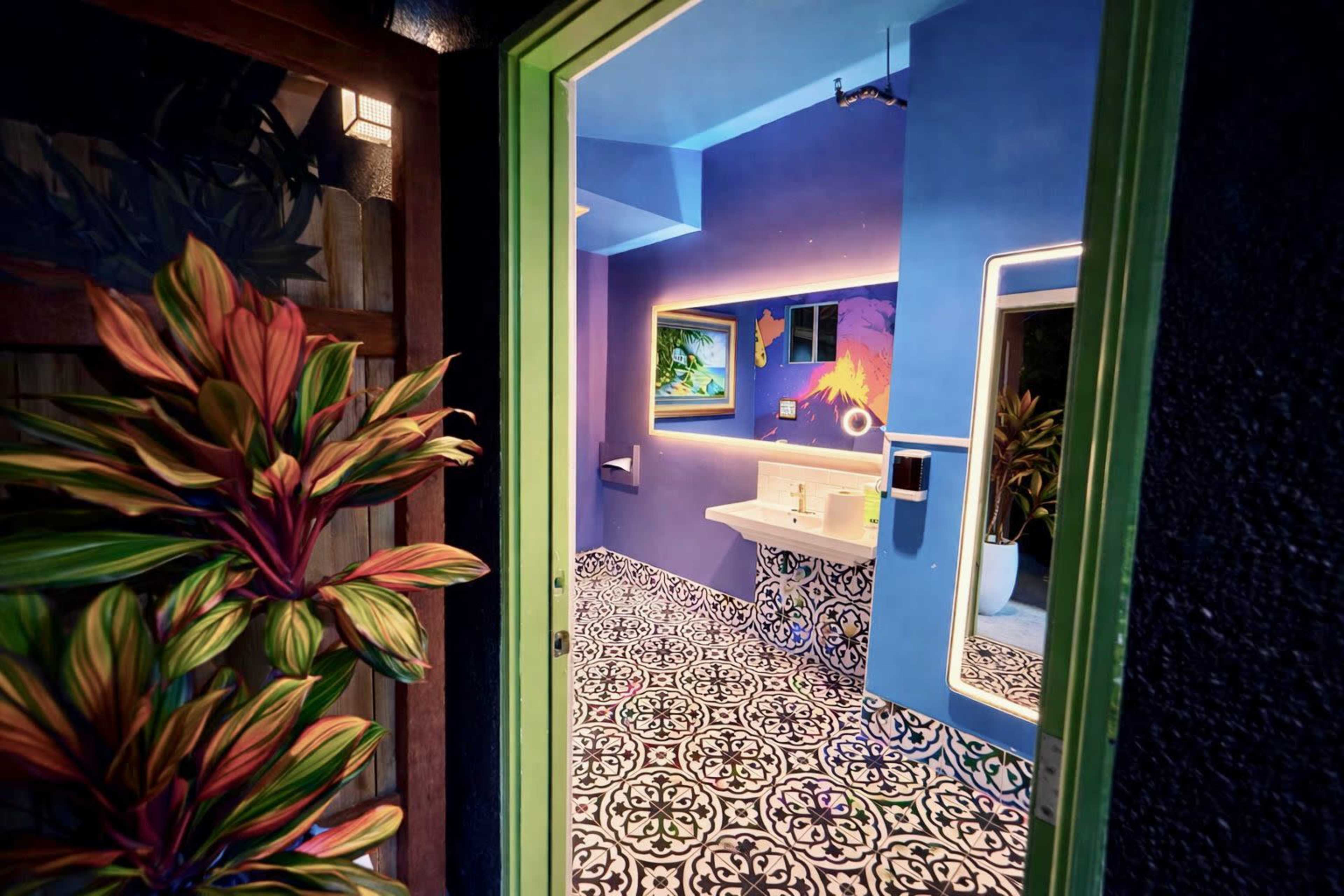 A brightly colored bathroom features a vibrant blue wall, patterned floor tiles, and a sink area illuminated by ambient lighting.