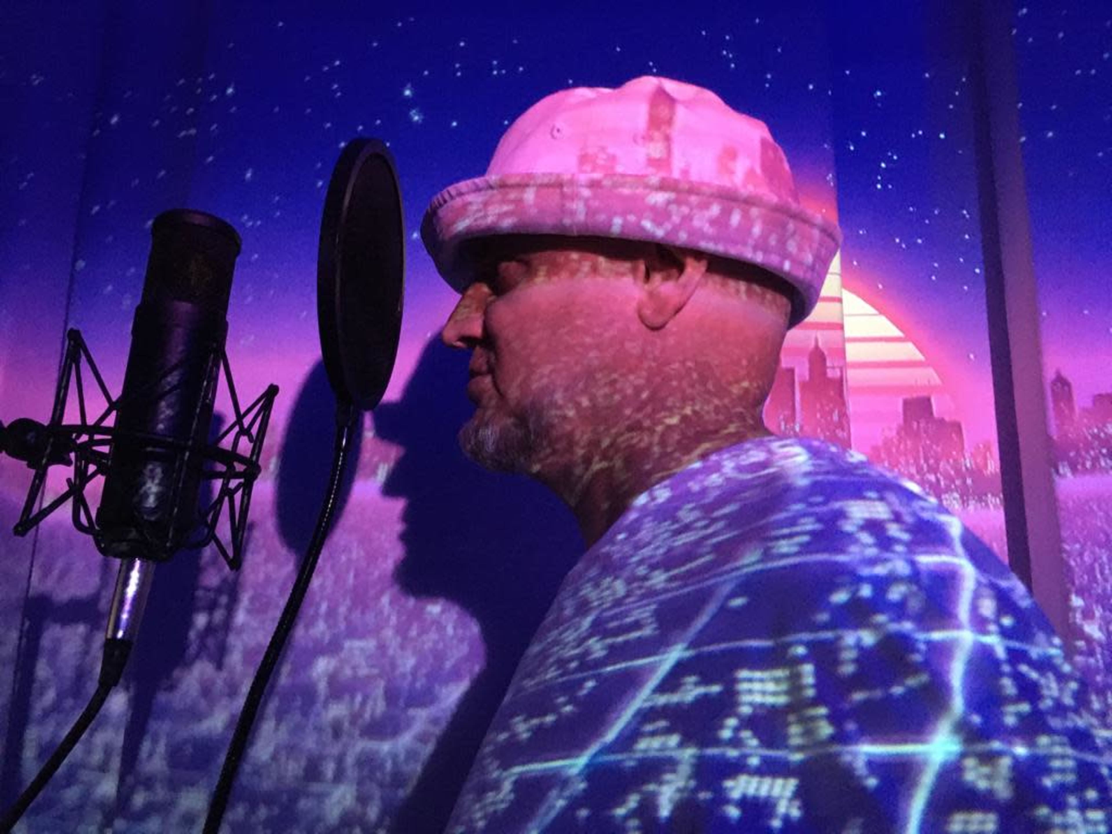 A man stands beside a microphone with a colorful cityscape projected onto his shirt and the wall behind him.