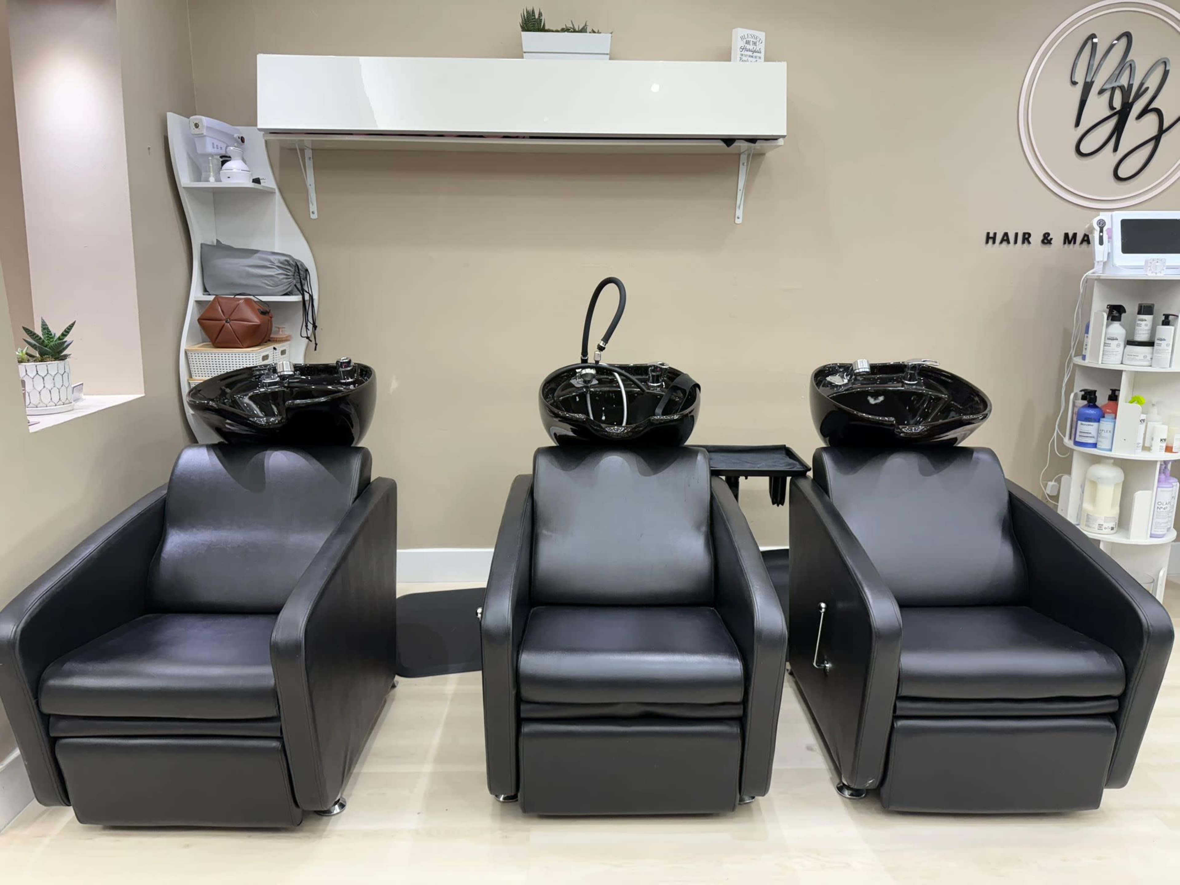The image shows three black salon chairs with washbasins set in a hair and makeup salon.