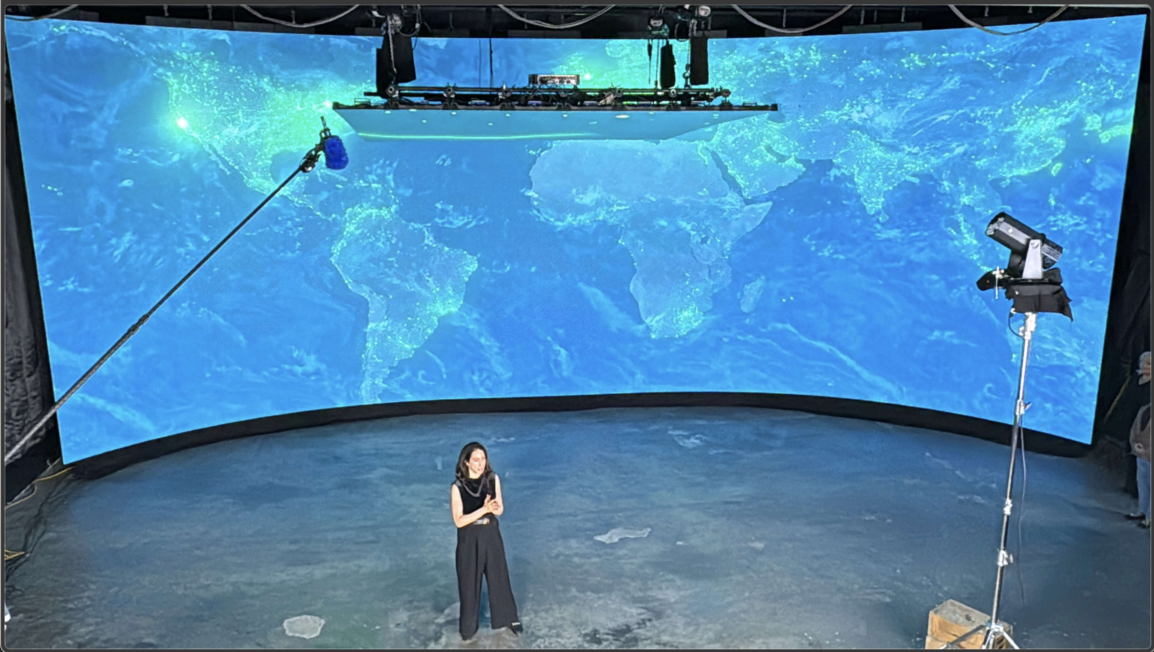 A woman stands in front of a large curved screen displaying a digitally rendered map of the world with highlighted areas.