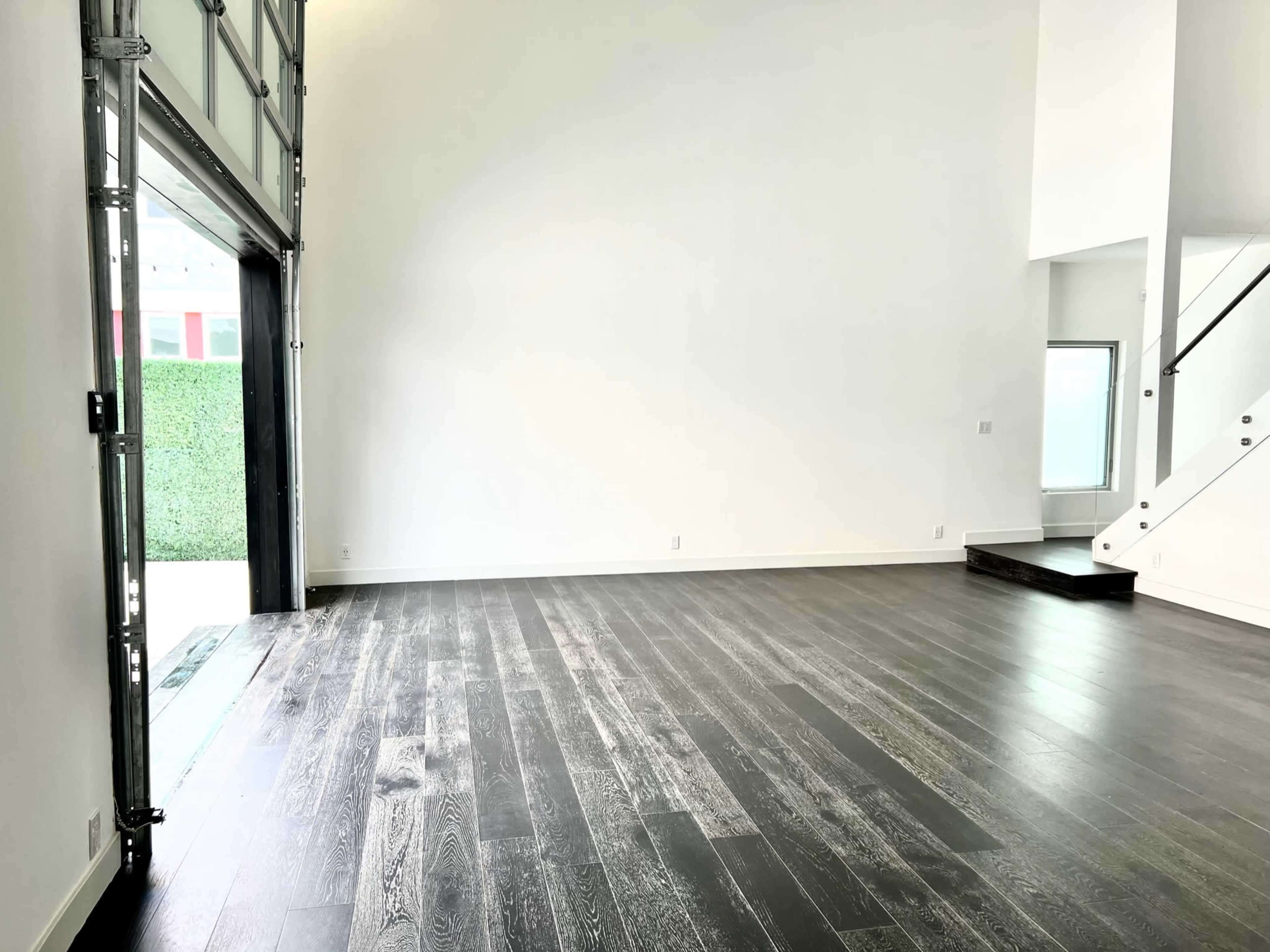 An empty room with hardwood floors and a large garage-style door opening to an outdoor space.