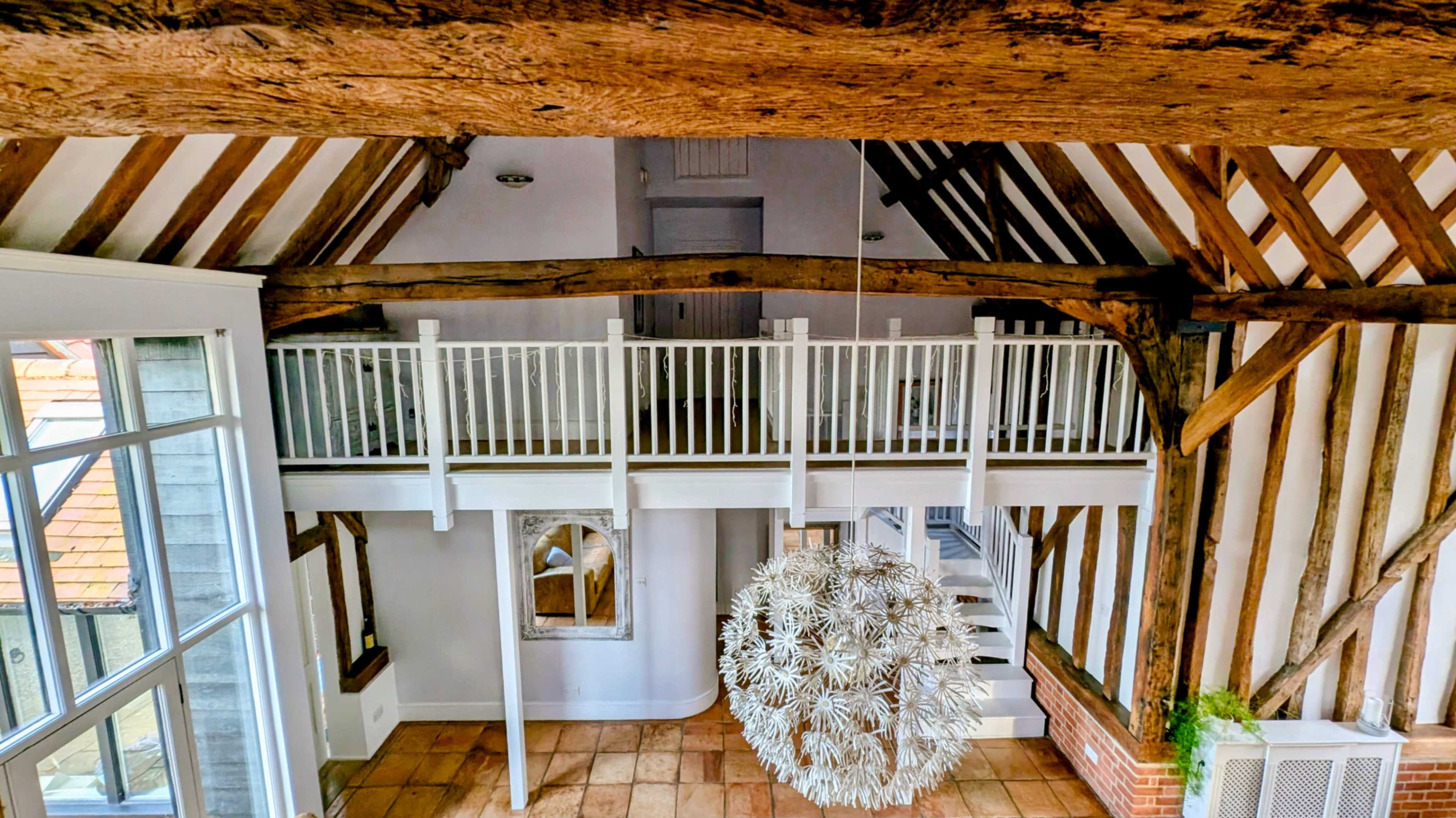 A spacious interior features exposed wooden beams, a loft area with a white railing, and a large spherical light fixture hanging from the ceiling.