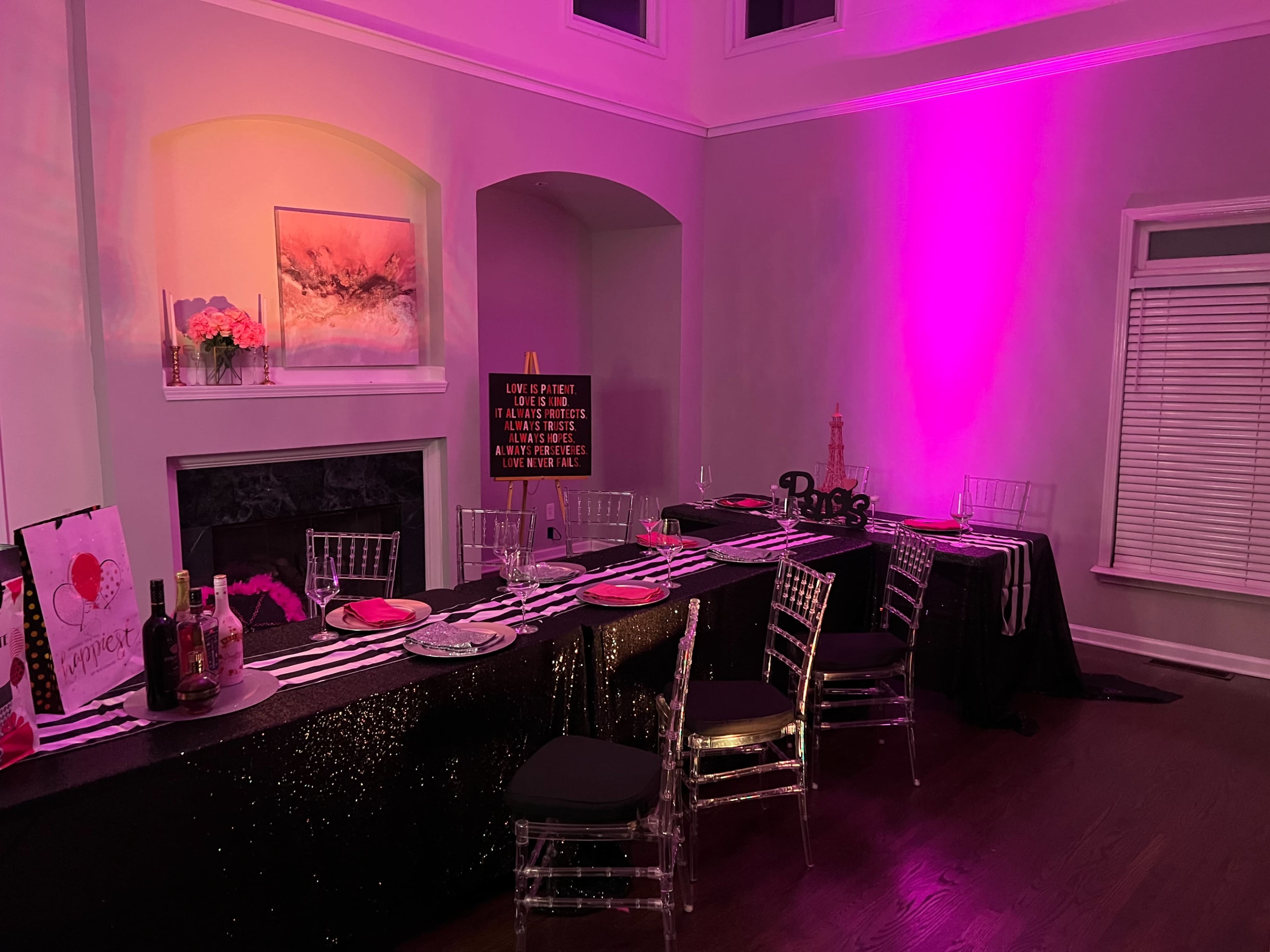 A dining area is set with a black and silver tablecloth, adorned with decorative items, and illuminated by pink lighting.