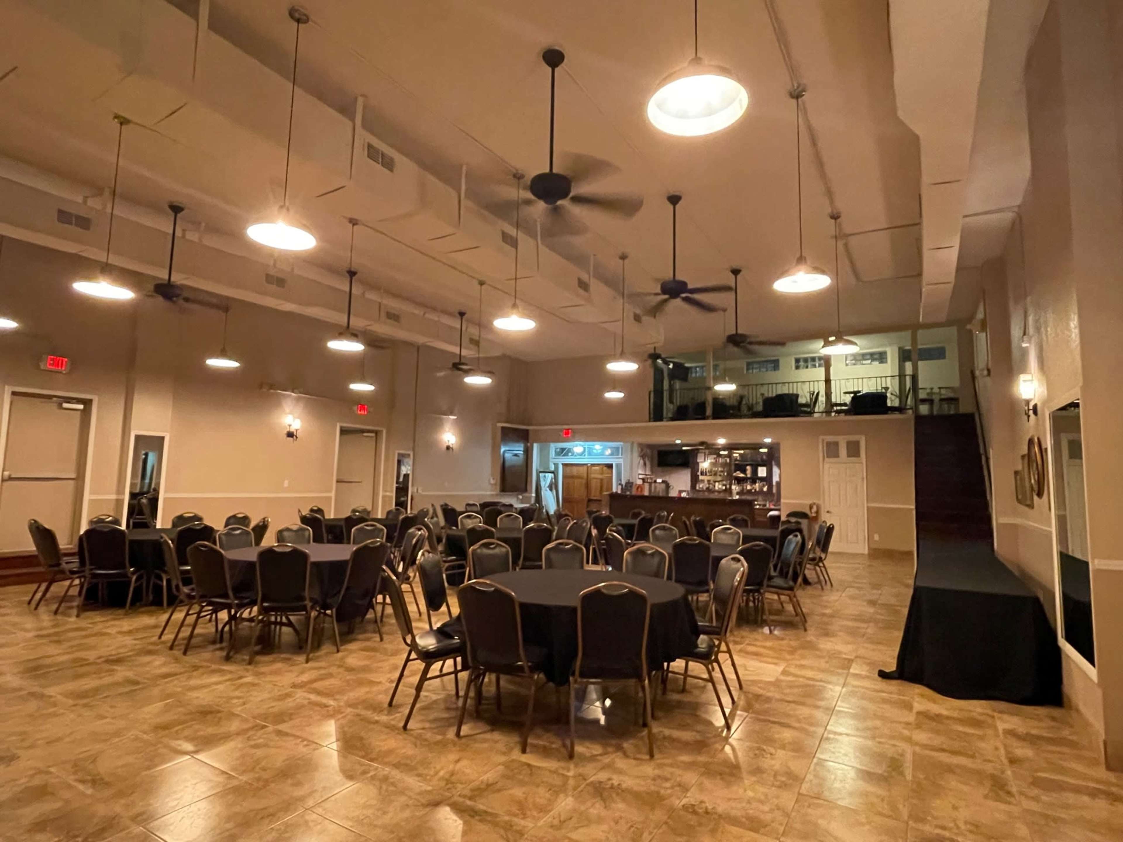 The image shows a spacious event hall with round tables set up and a stage area at one end.