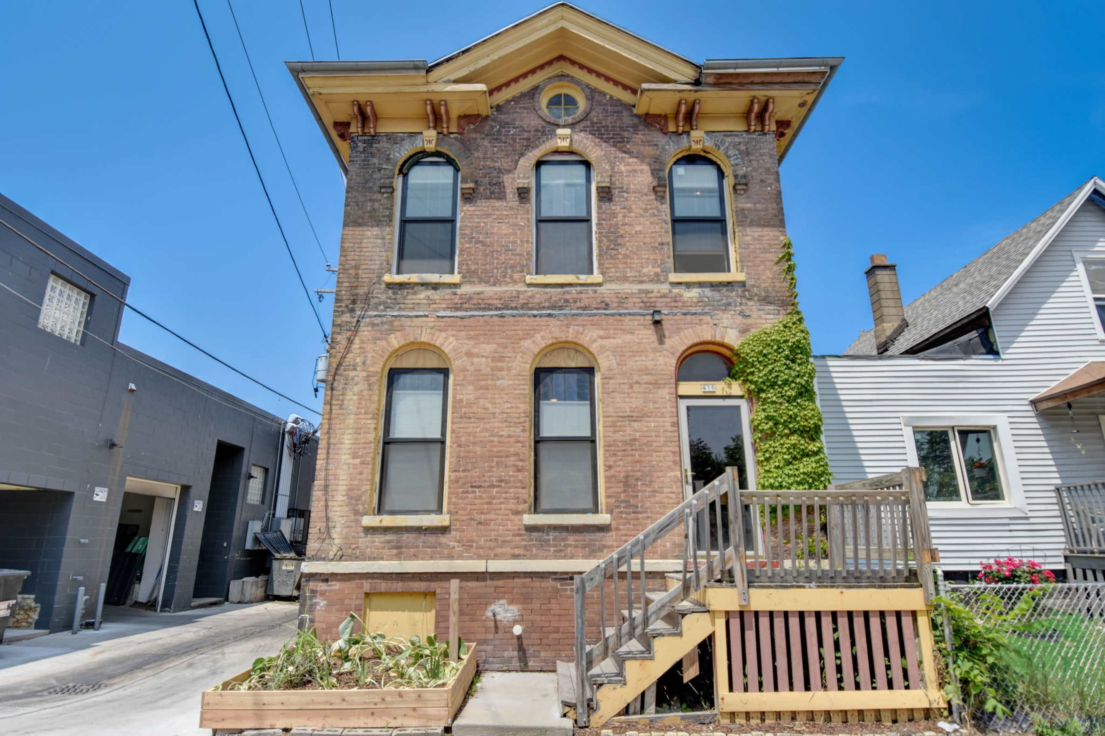 A three-story brick building with large windows, a staircase leading to the entrance, and vines climbing one side.