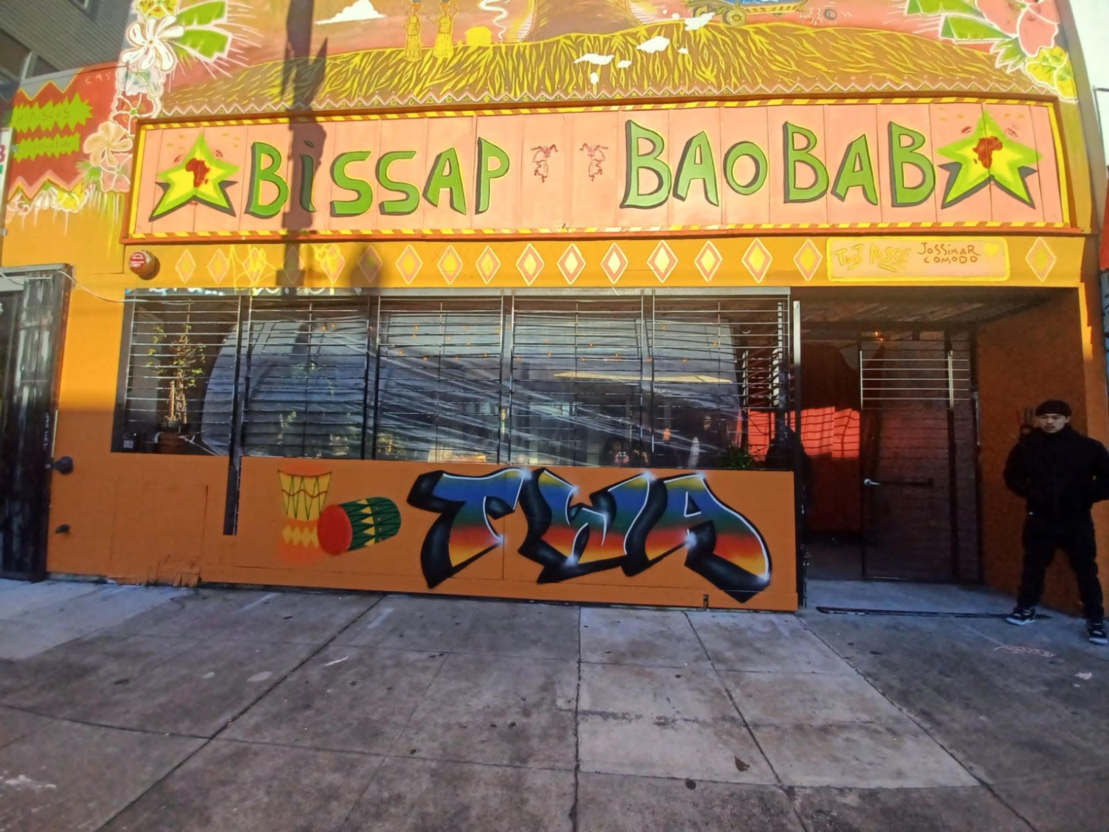 The vibrant storefront of a restaurant named "Bissap Baobab," featuring colorful murals and a graffiti-style artwork on a panel.