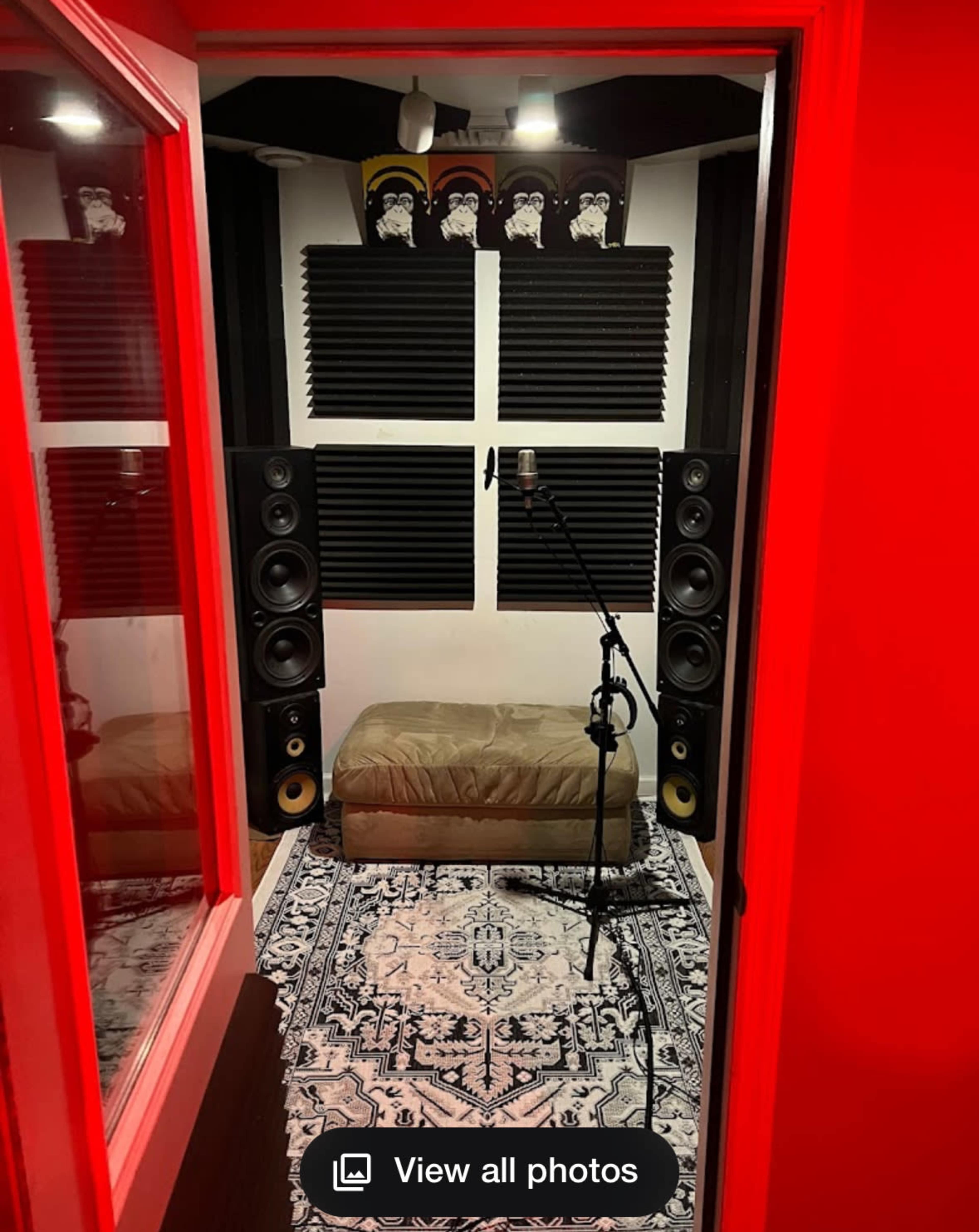 The image shows a small recording studio with soundproofing panels on the walls, a microphone on a stand, and large speakers positioned nearby, all surrounded by a red frame.