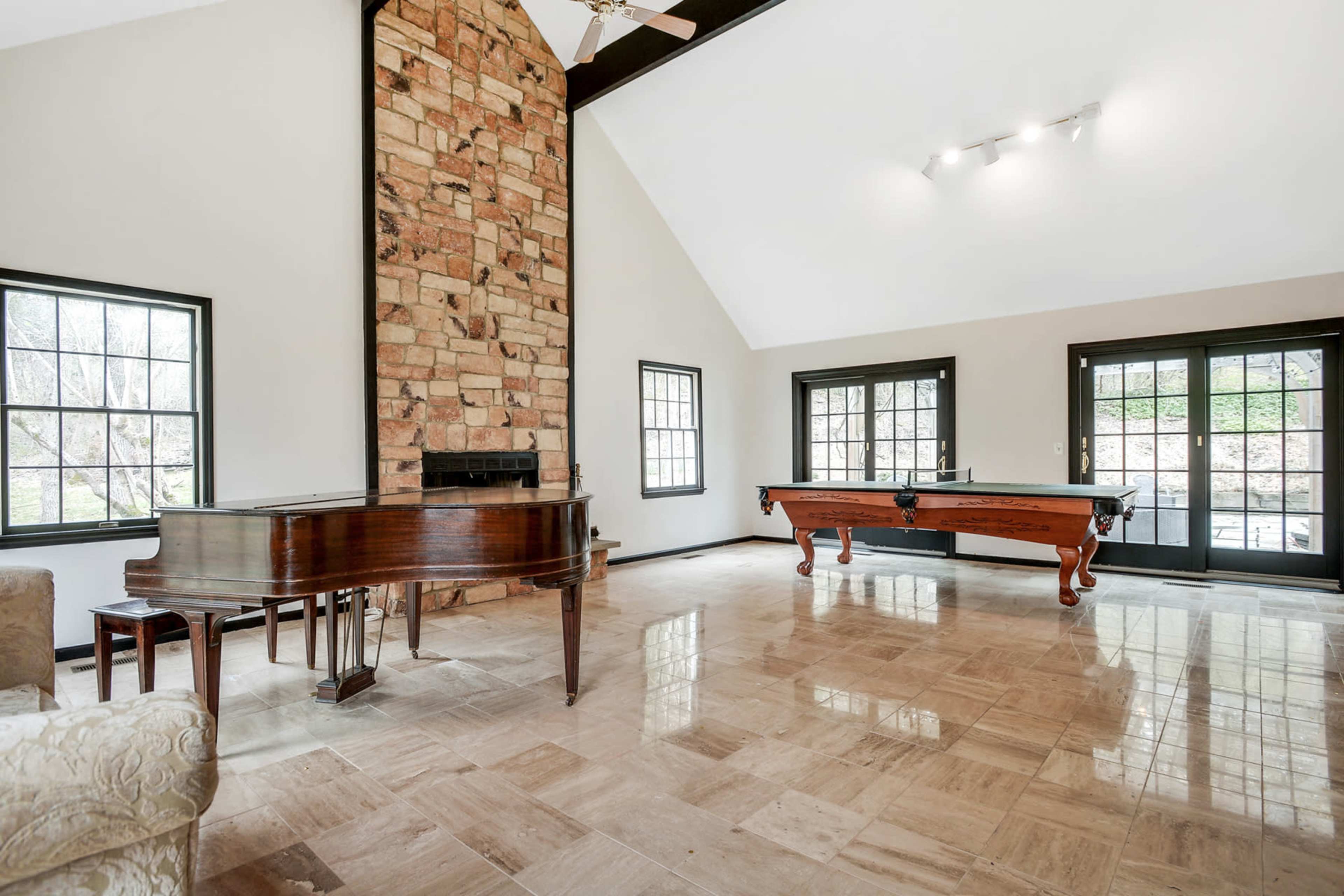 A spacious living area features a grand piano and a billiard table, flanked by large windows and a stone fireplace.