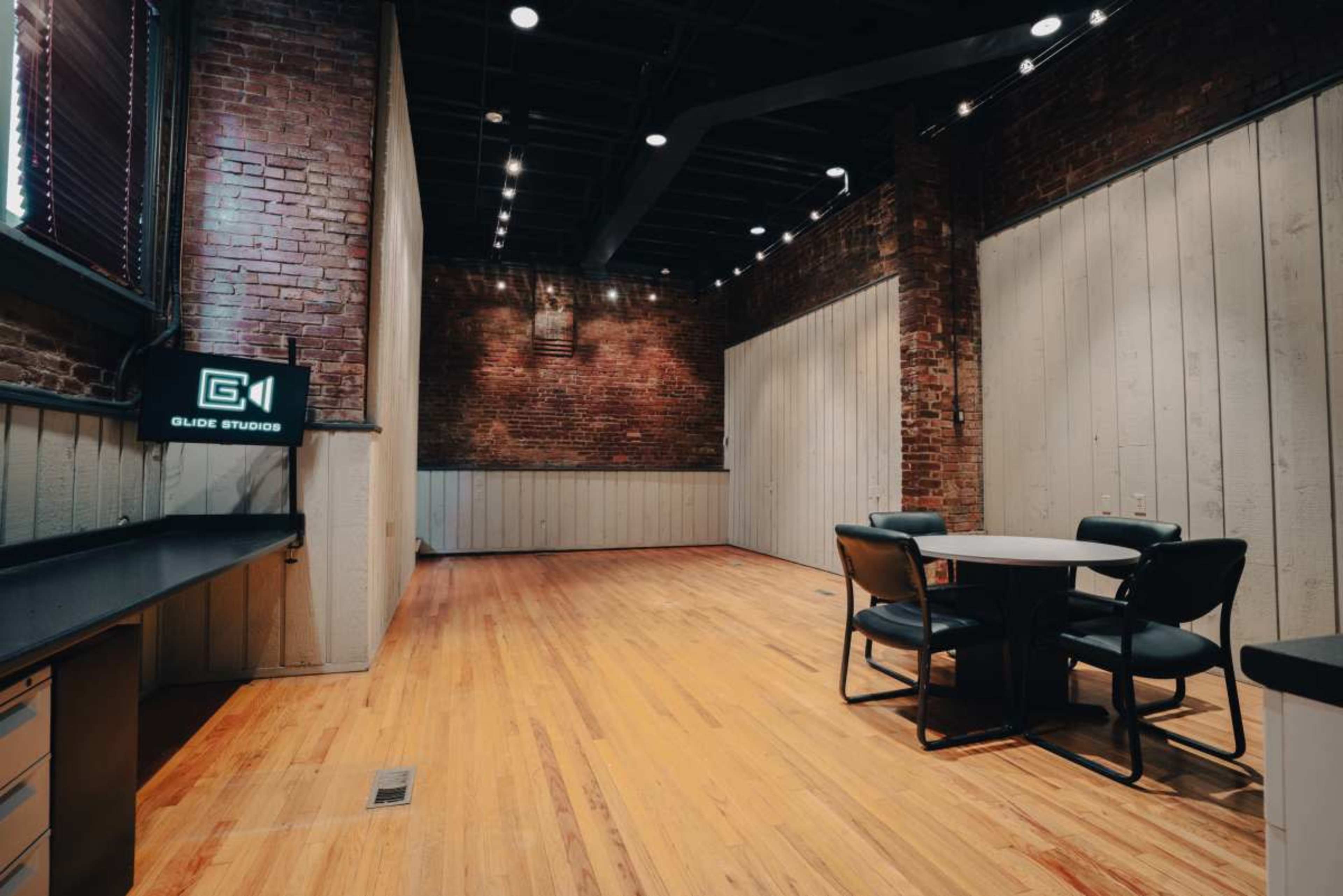 A spacious studio with exposed brick walls, wooden flooring, and a round table surrounded by four chairs.