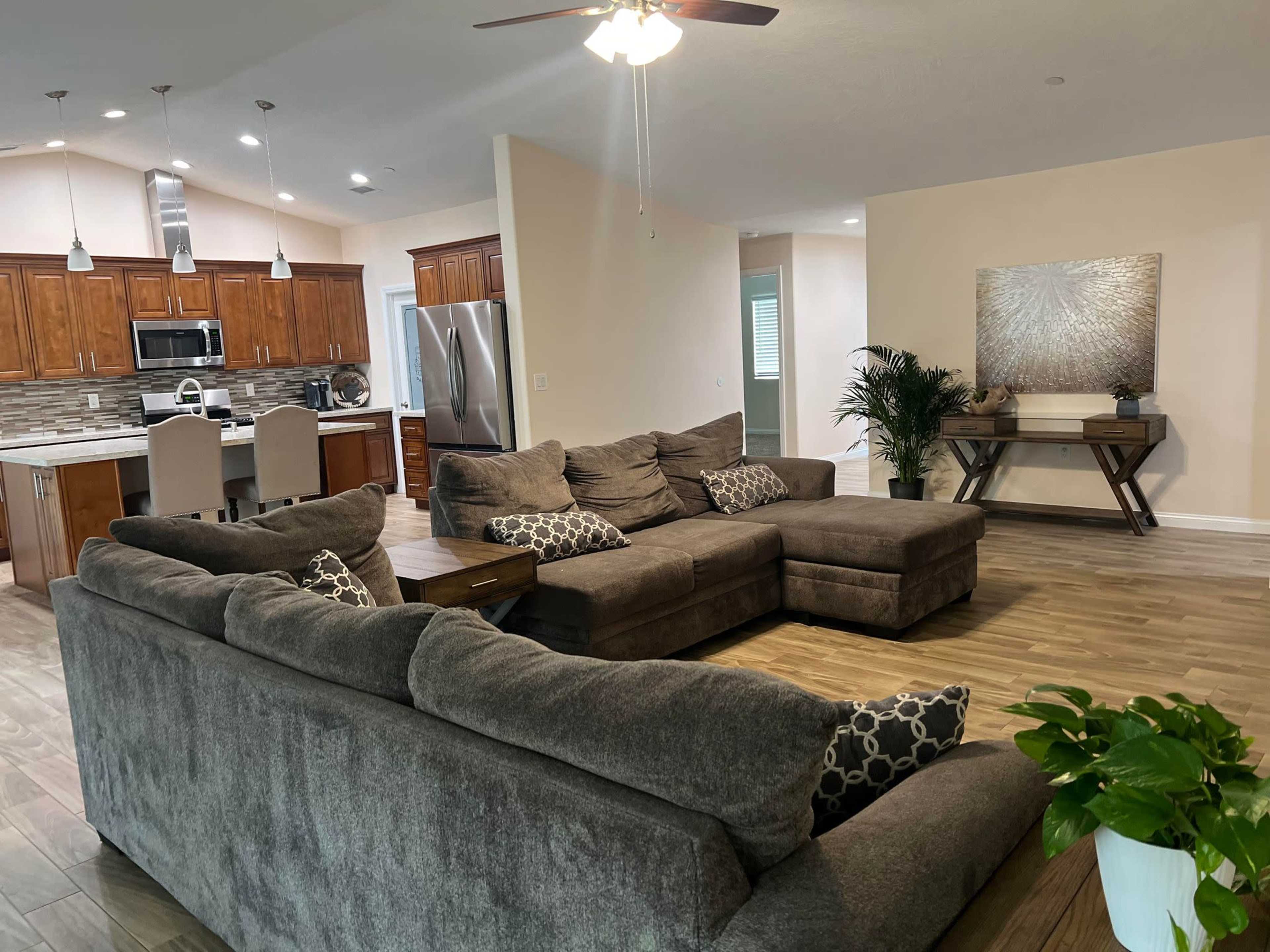 A spacious living area with a large sectional sofa, a coffee table, and a view of a modern kitchen in the background.