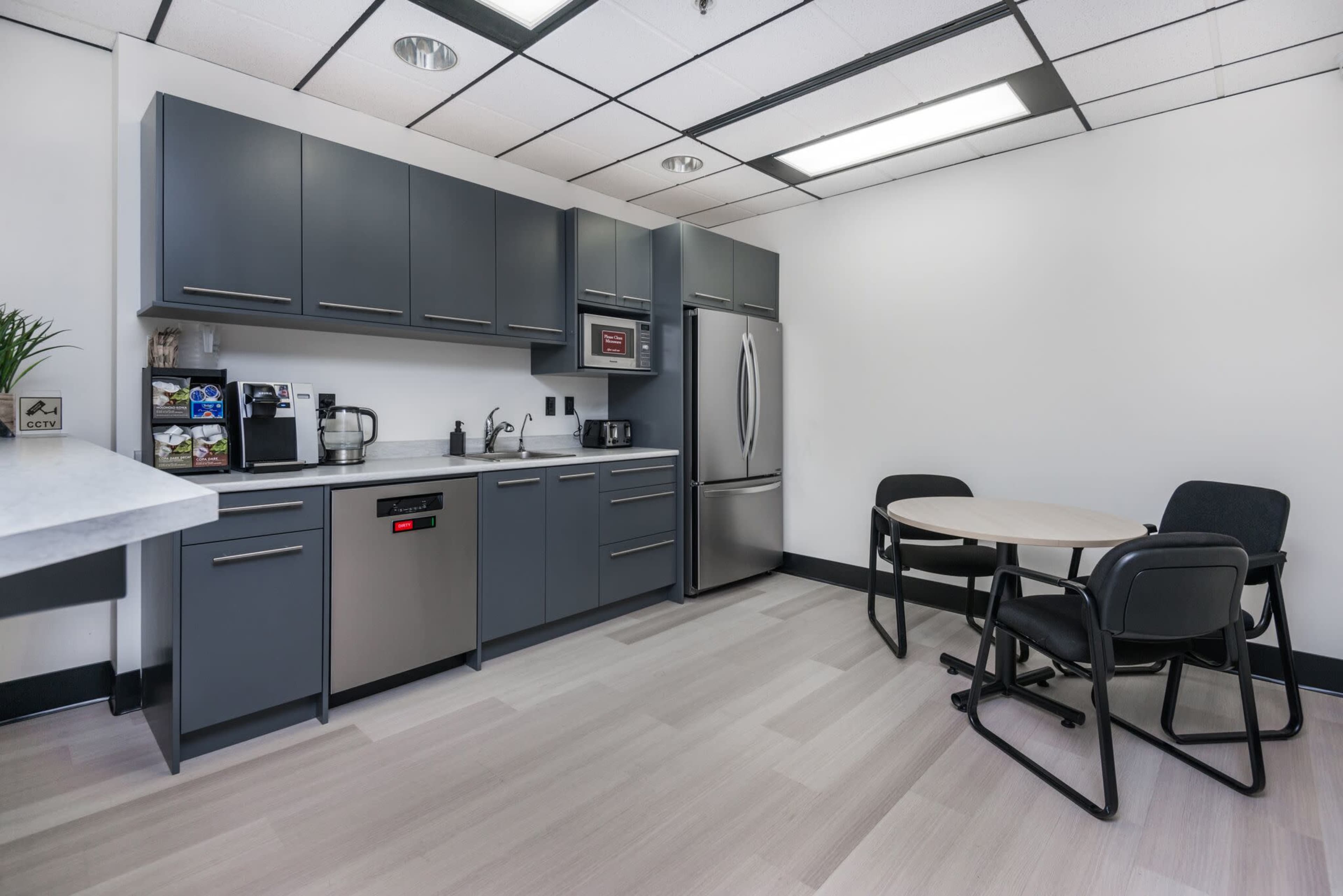 A modern kitchen area with dark cabinets, stainless steel appliances, and a round table with black chairs.