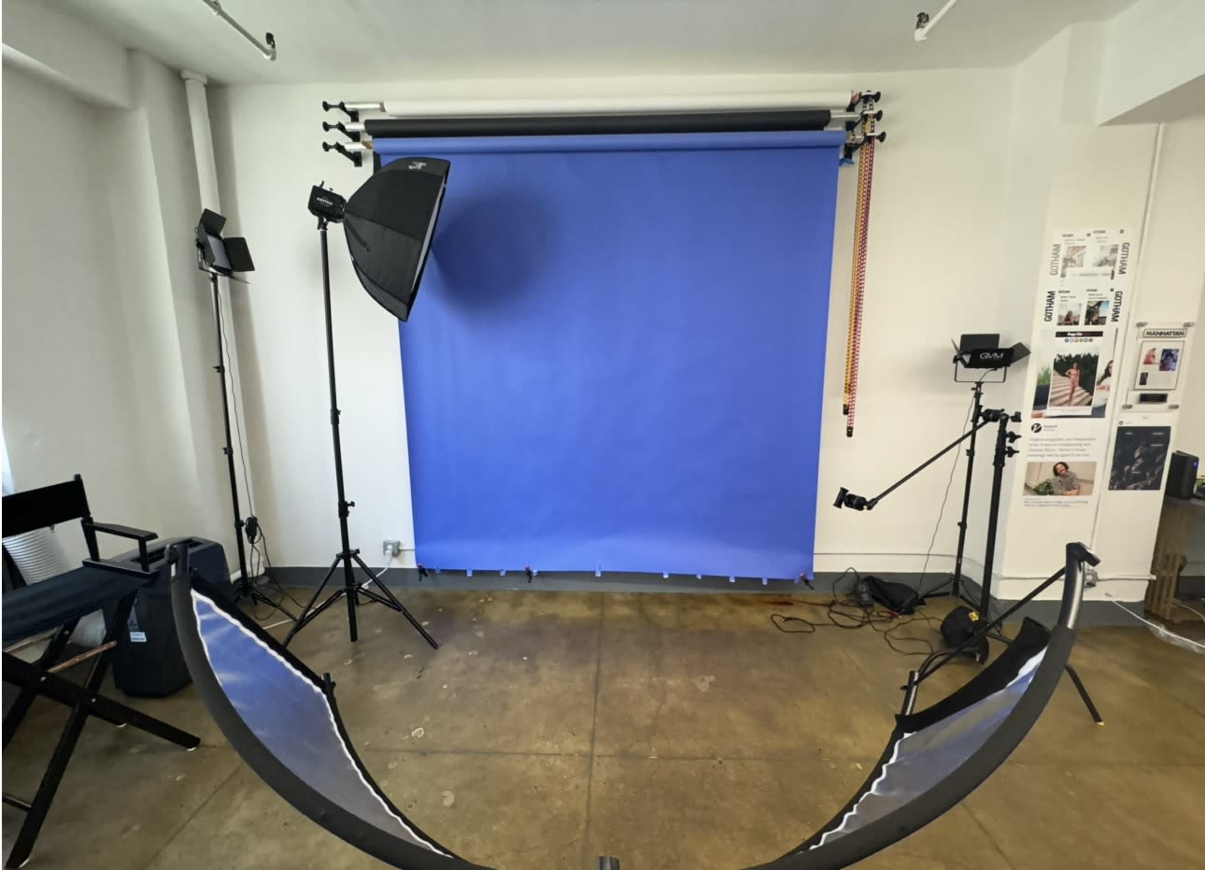 A photography studio setup with a blue backdrop, lighting equipment, and a director's chair.