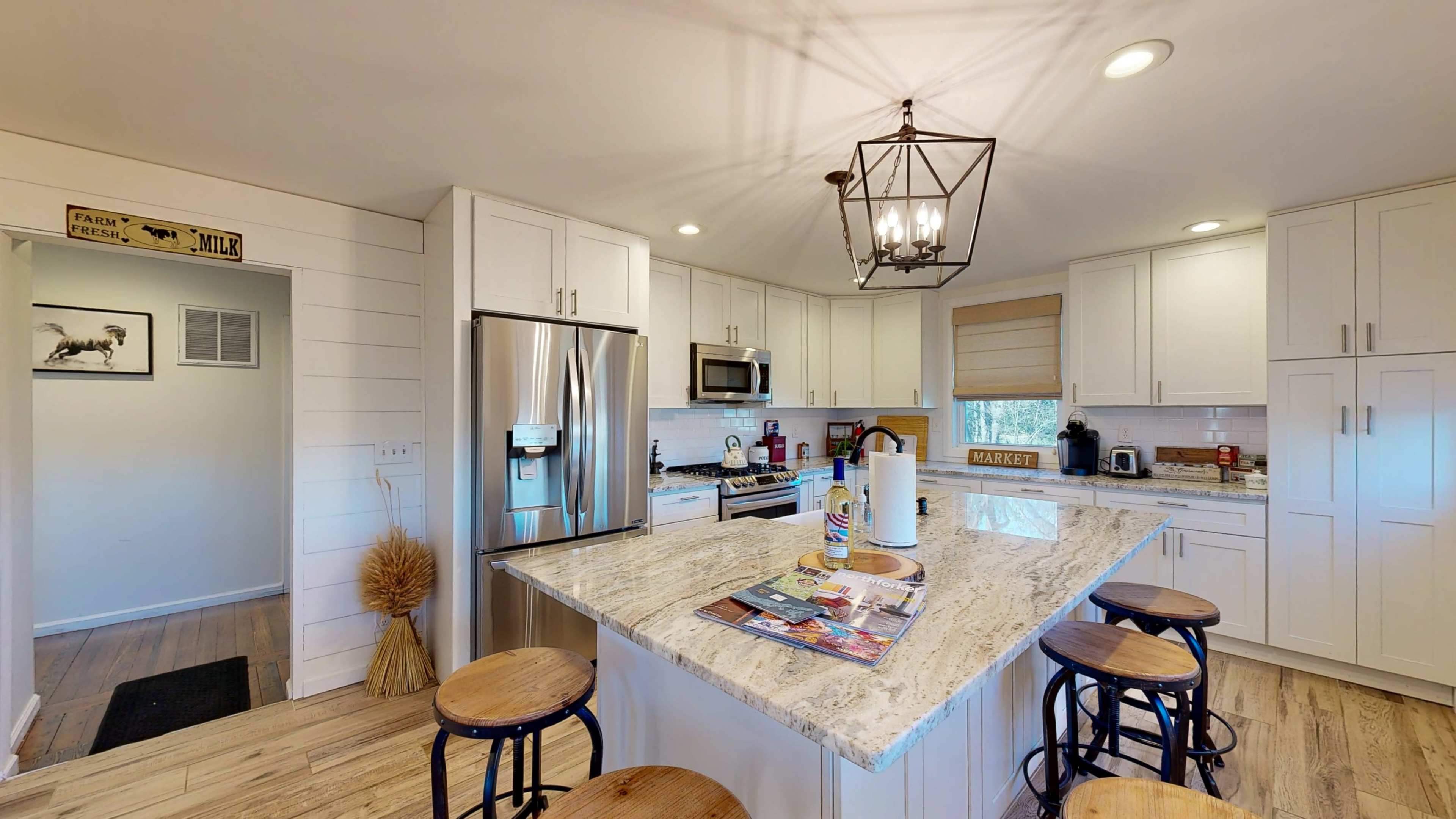 The kitchen features white cabinetry, a large granite island with bar stools, and stainless steel appliances.