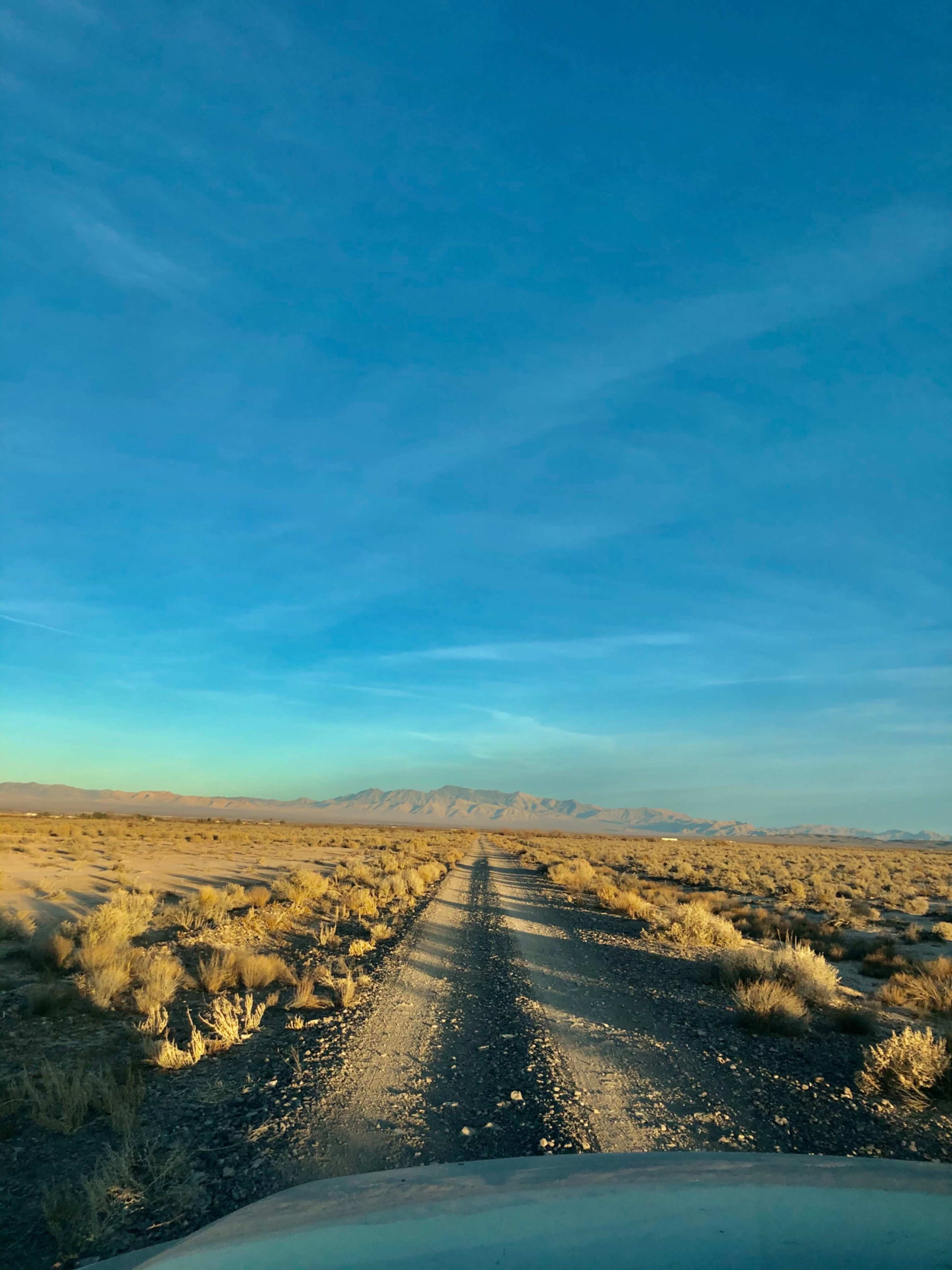 A gravel road stretches through a vast, open landscape under a clear blue sky.
