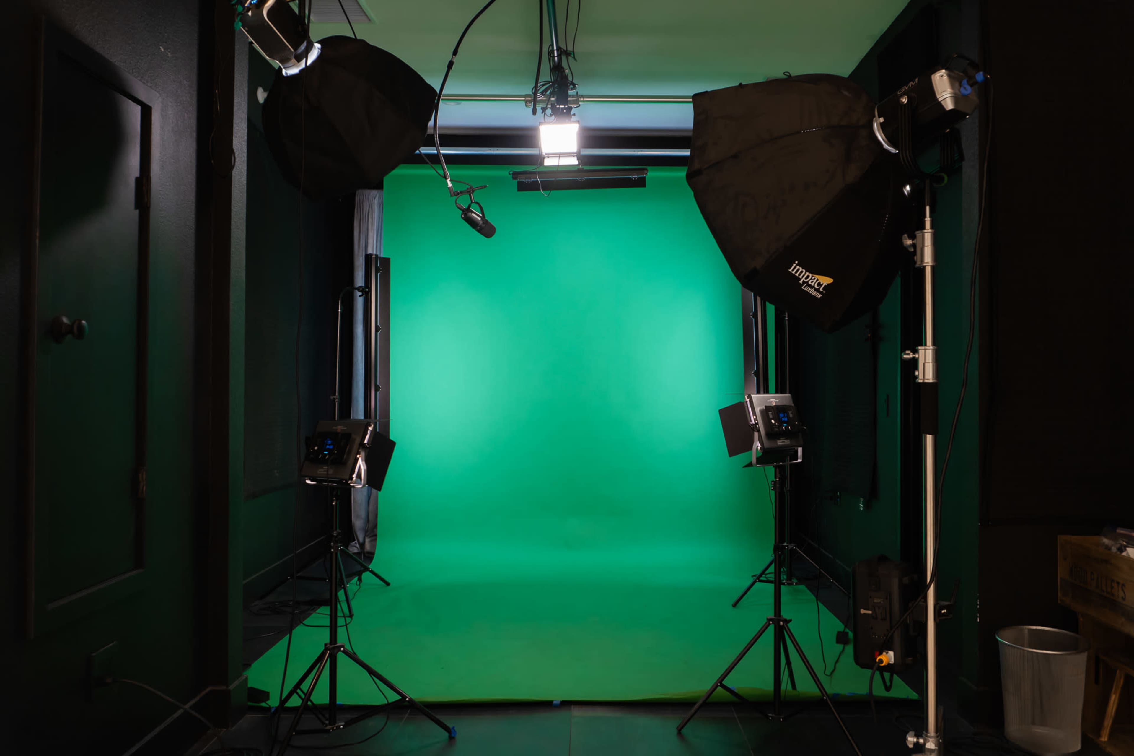 The image shows a photography studio featuring a green screen backdrop, with several studio lights positioned in front of it.