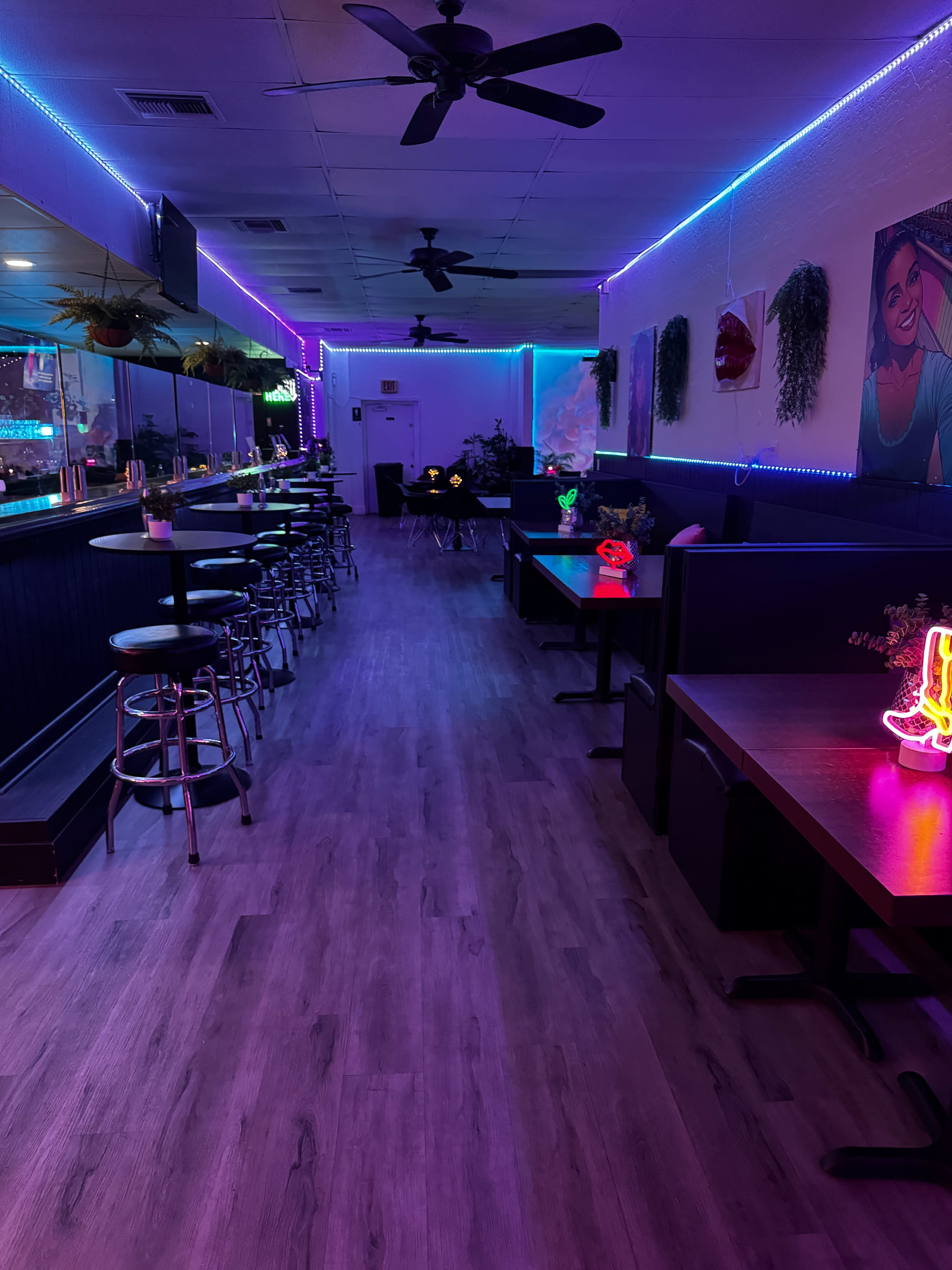 The image depicts an interior view of a modern restaurant or bar with neon lighting, featuring tables, chairs, and a long bar area along one side.