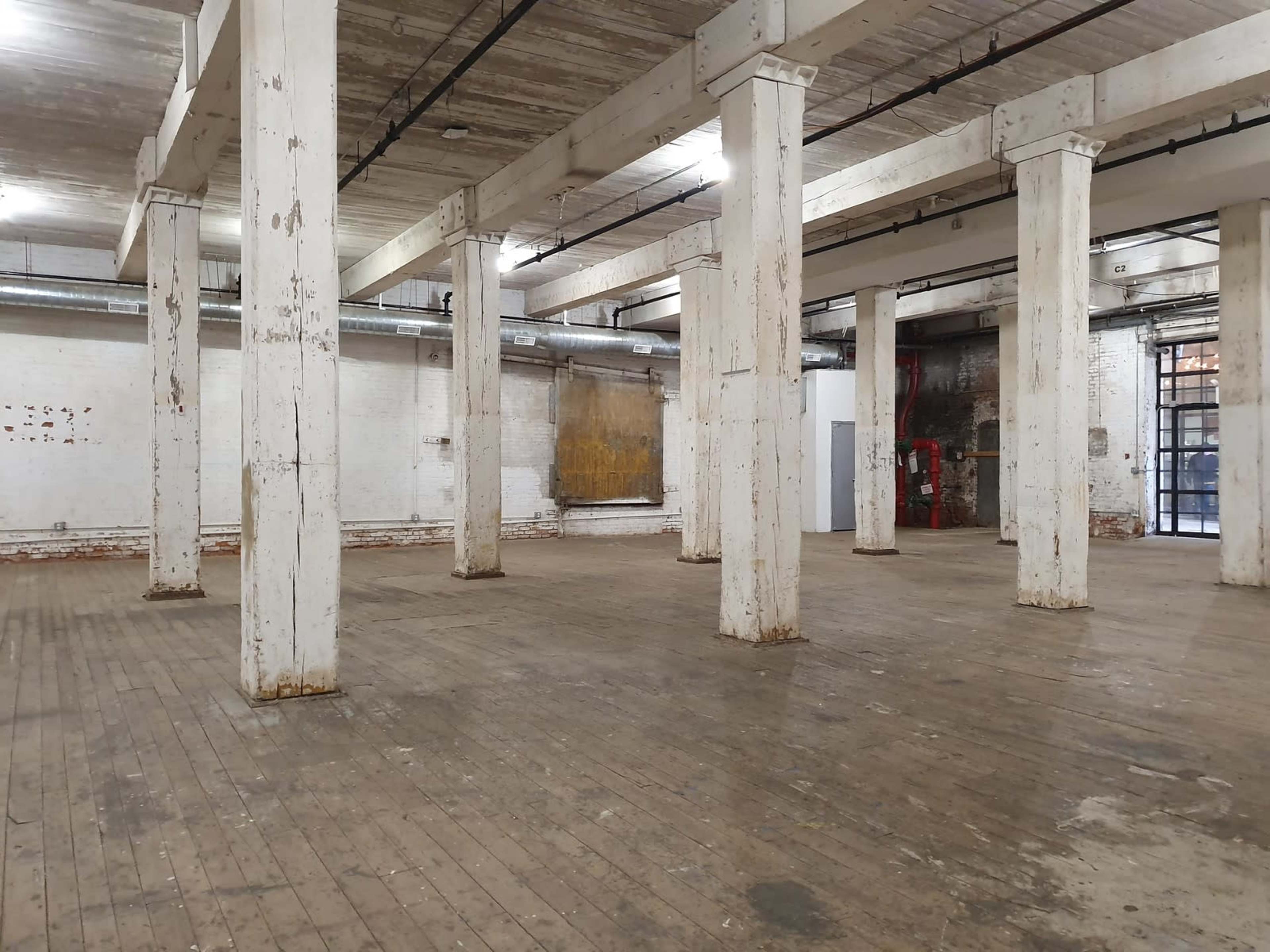 An empty industrial space with wooden flooring and several large white pillars.