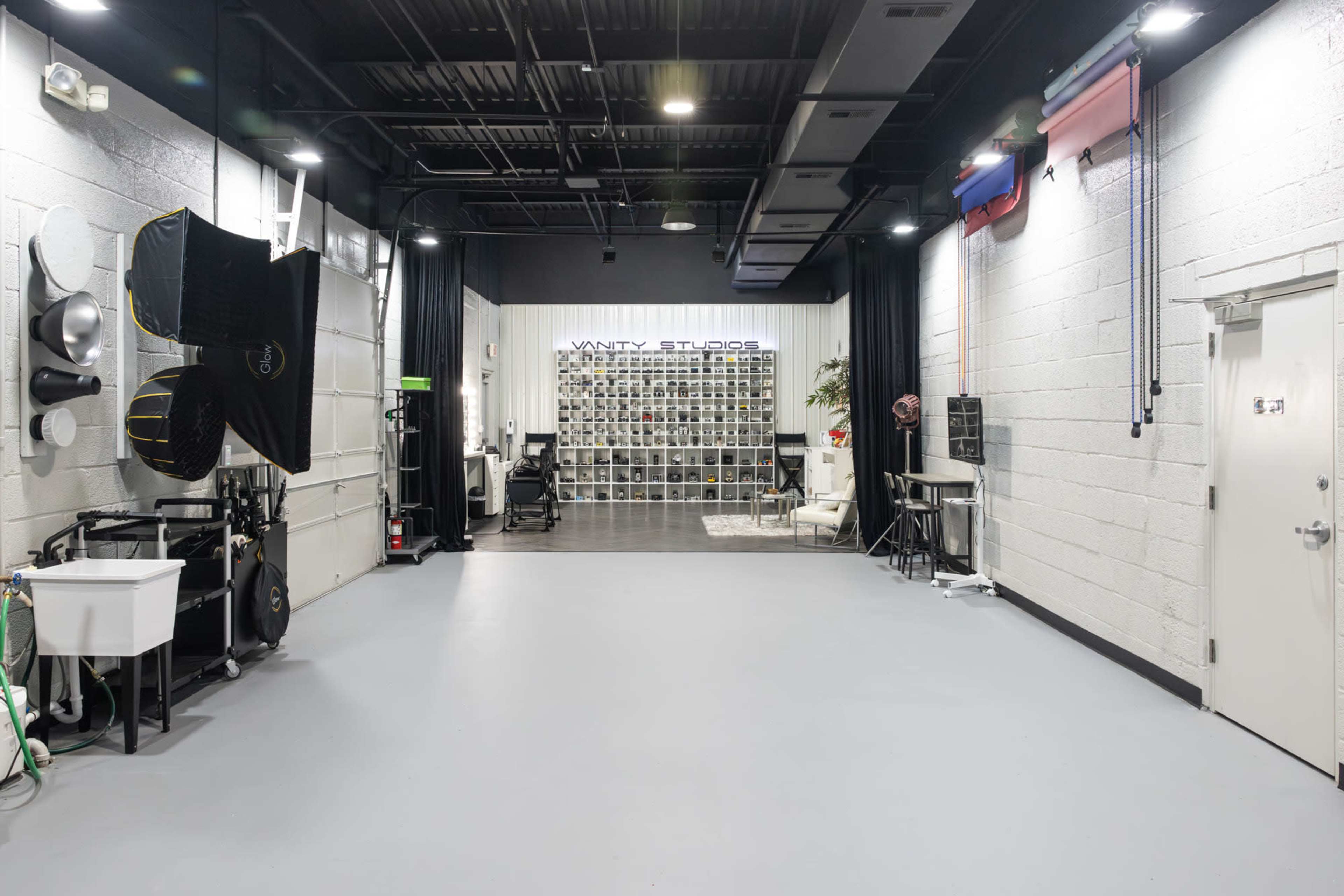 A spacious studio interior with lighting equipment, backdrops, and a wall of organized shelves.