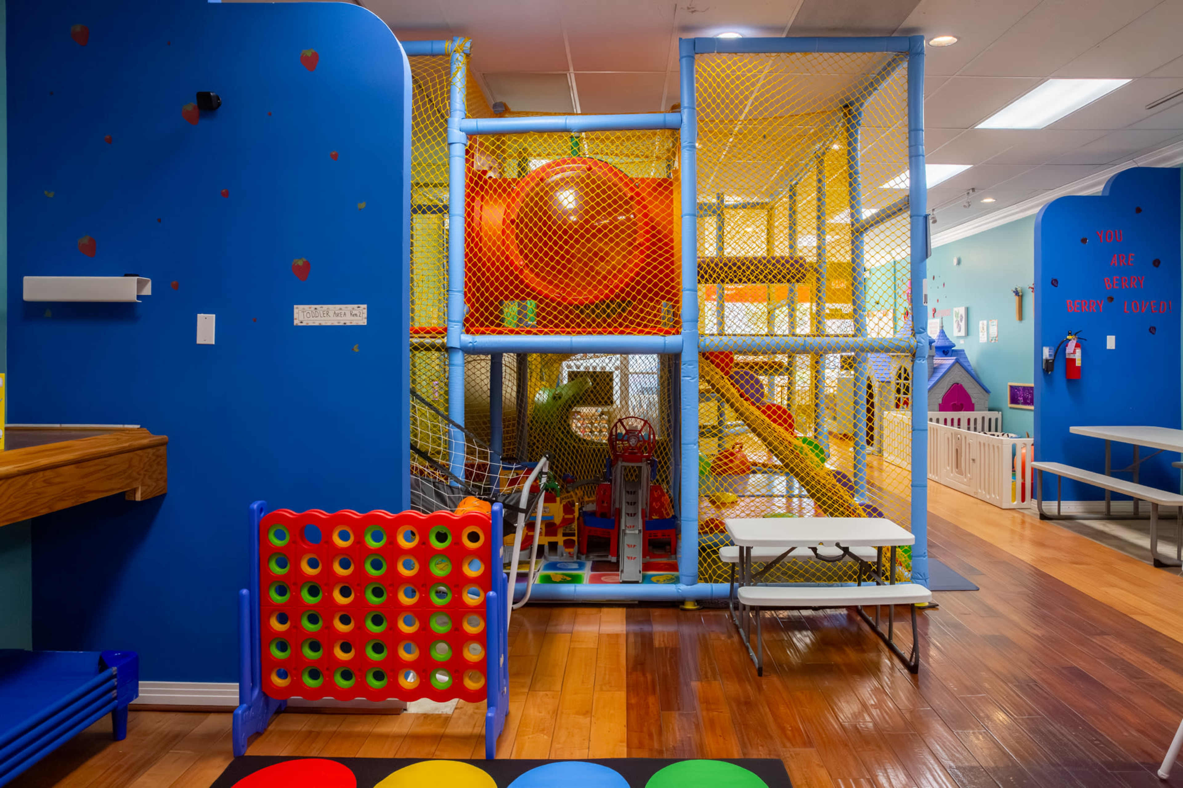 The image shows an indoor playground with colorful play structures, slides, and climbing equipment, enclosed in a safety net.