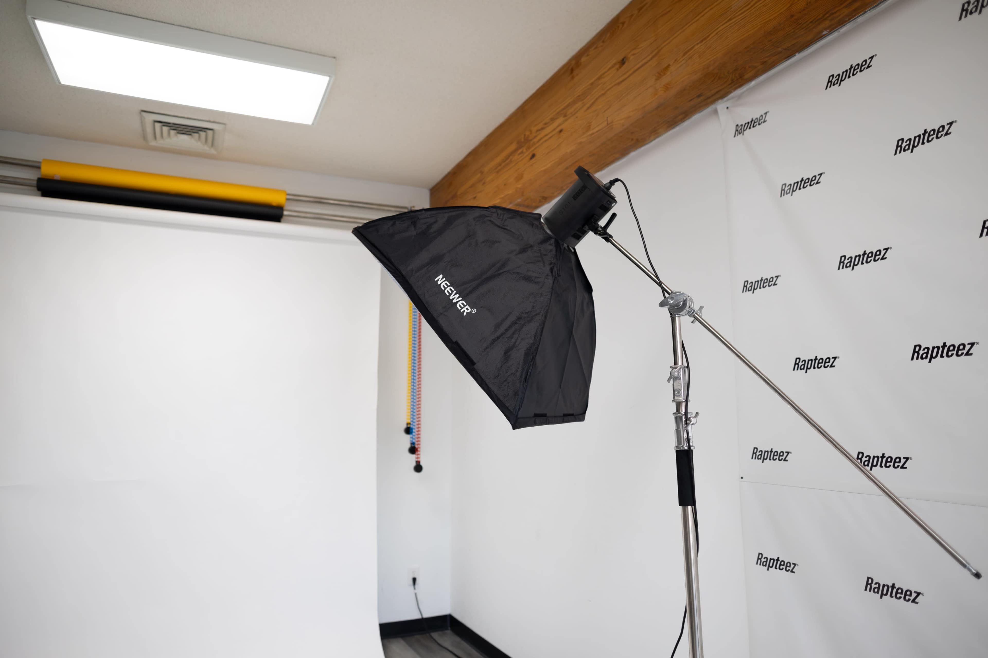 The image shows a photography studio setup with a light softbox mounted on a stand, positioned near a white backdrop.