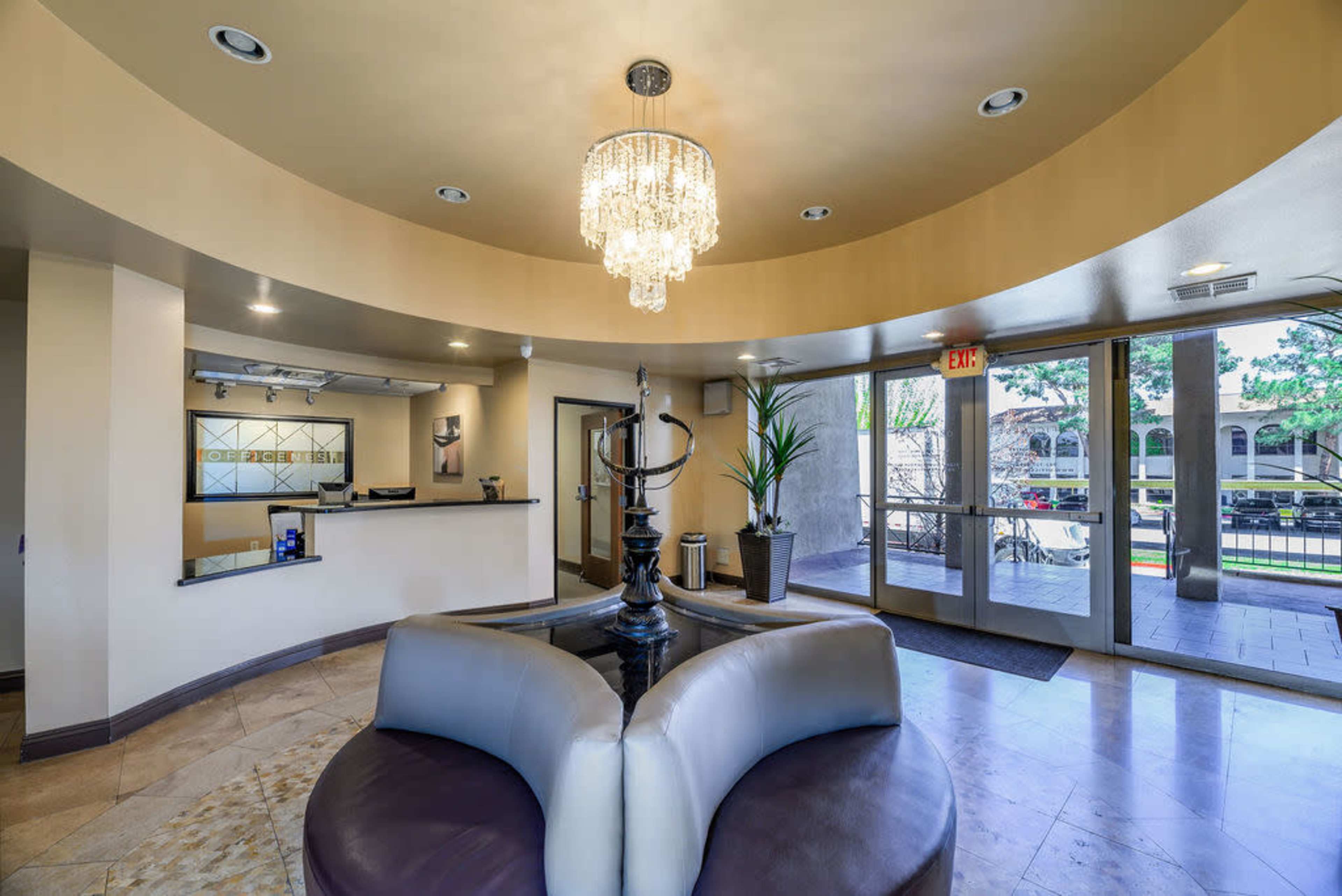 A modern lobby featuring a central fountain, a chandelier, a reception desk, and large windows allowing natural light.