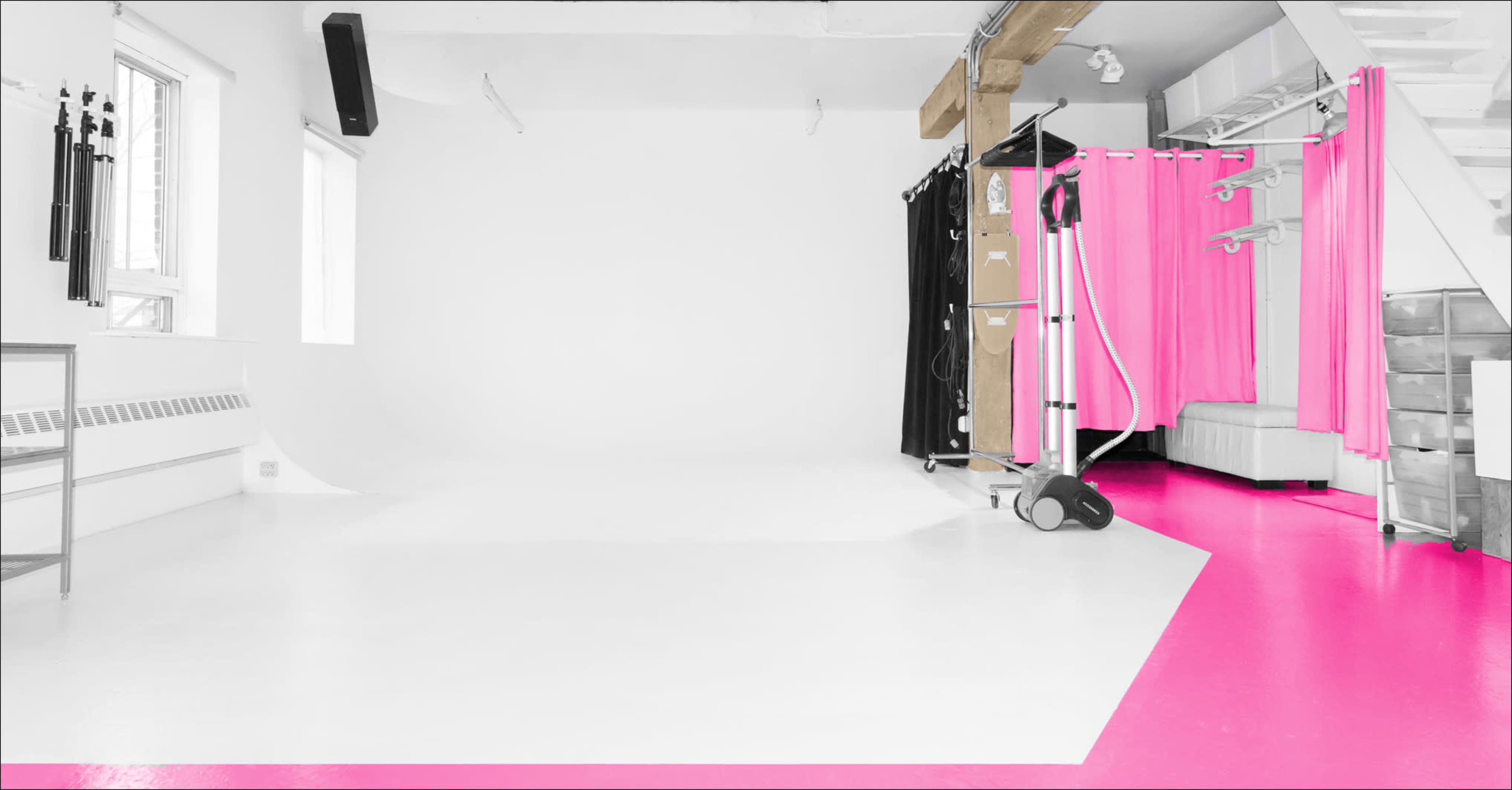 A photo studio with a white backdrop, pink flooring, and various props including black and pink curtains.