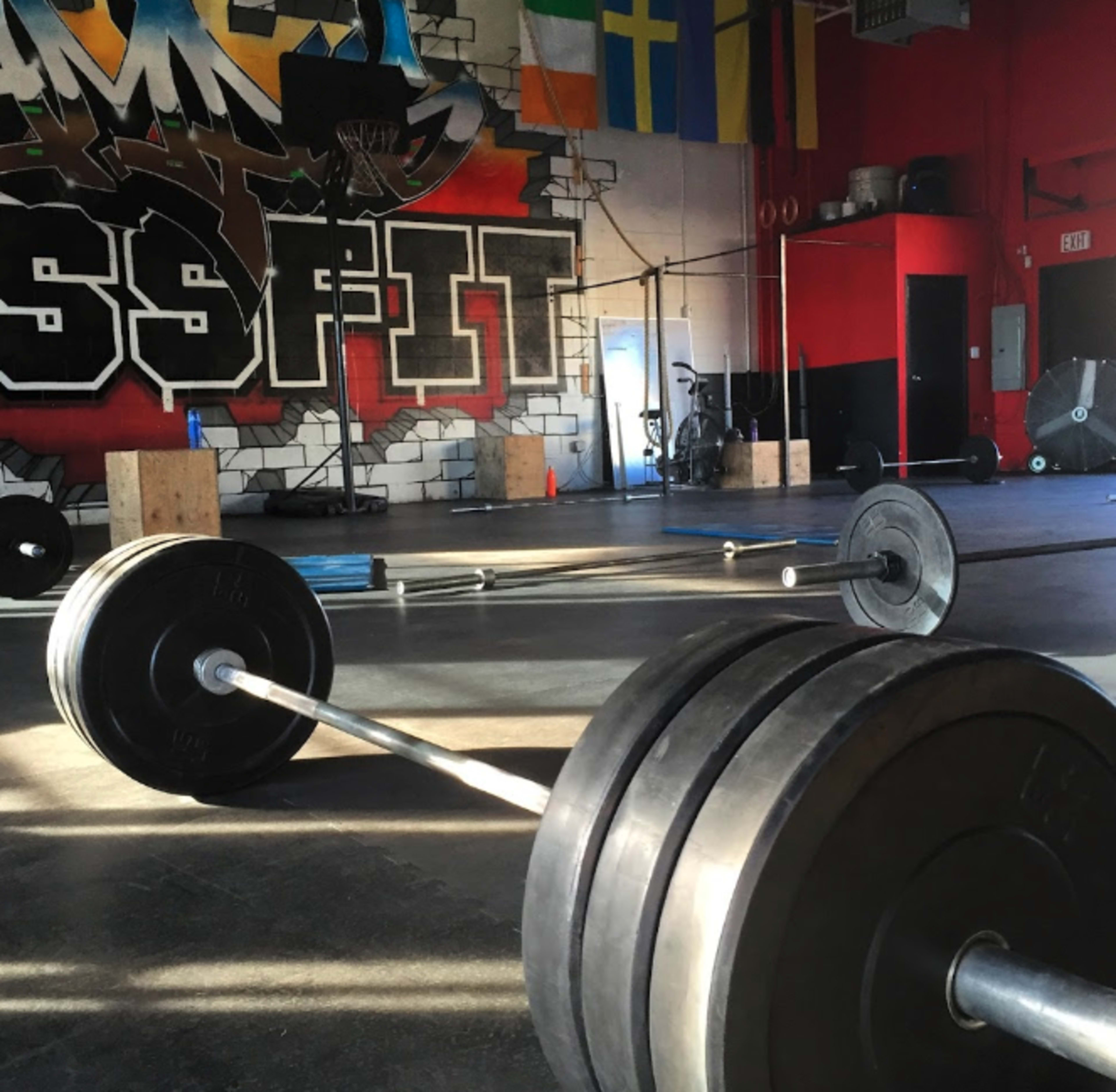 A gym floor with barbell weights scattered around against a backdrop of a colorful mural and various gym equipment.