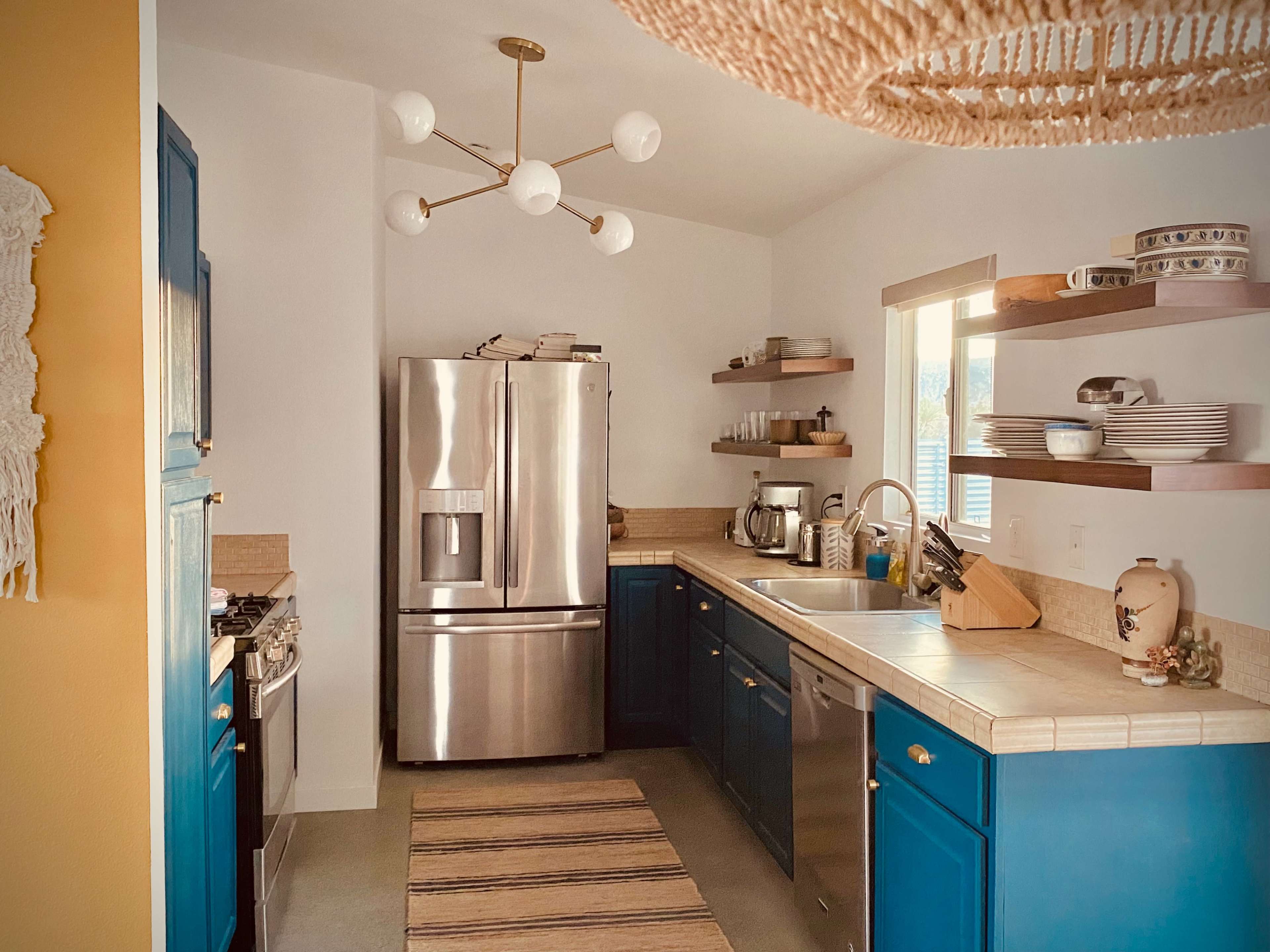 The kitchen features stainless steel appliances, blue cabinetry, and open shelves displaying dishware.