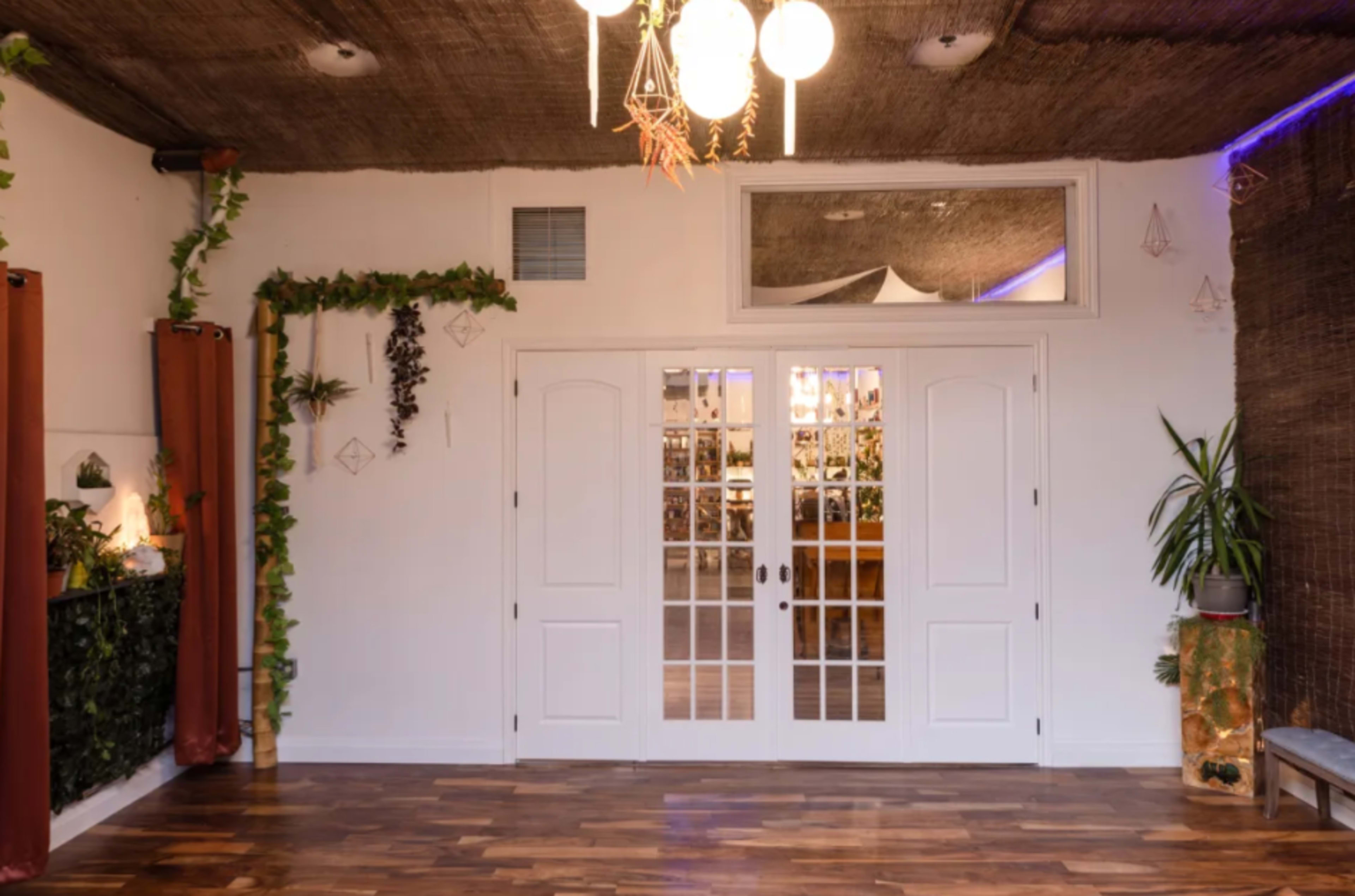 A bright room with wooden flooring, French double doors at the center, and greenery decorations along the walls.